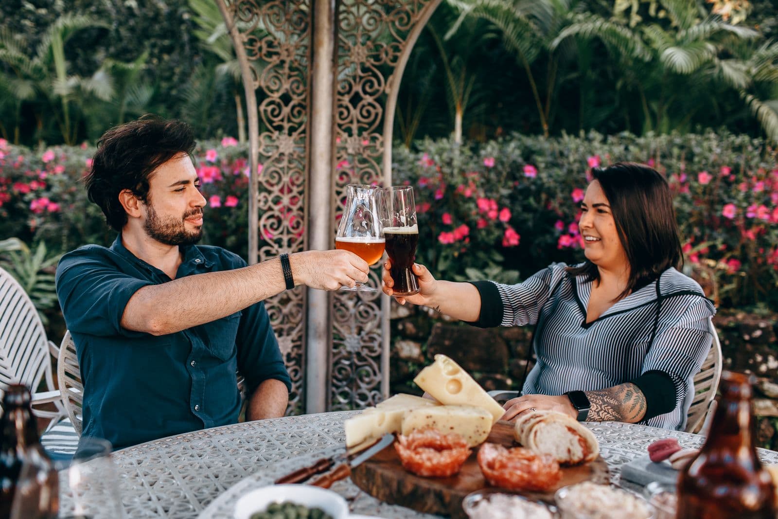 Twee mensen proosten met een glas aan een tafel in een tuin vol bloemen, een warm beeld bij een vijftigste verjaardag vieren