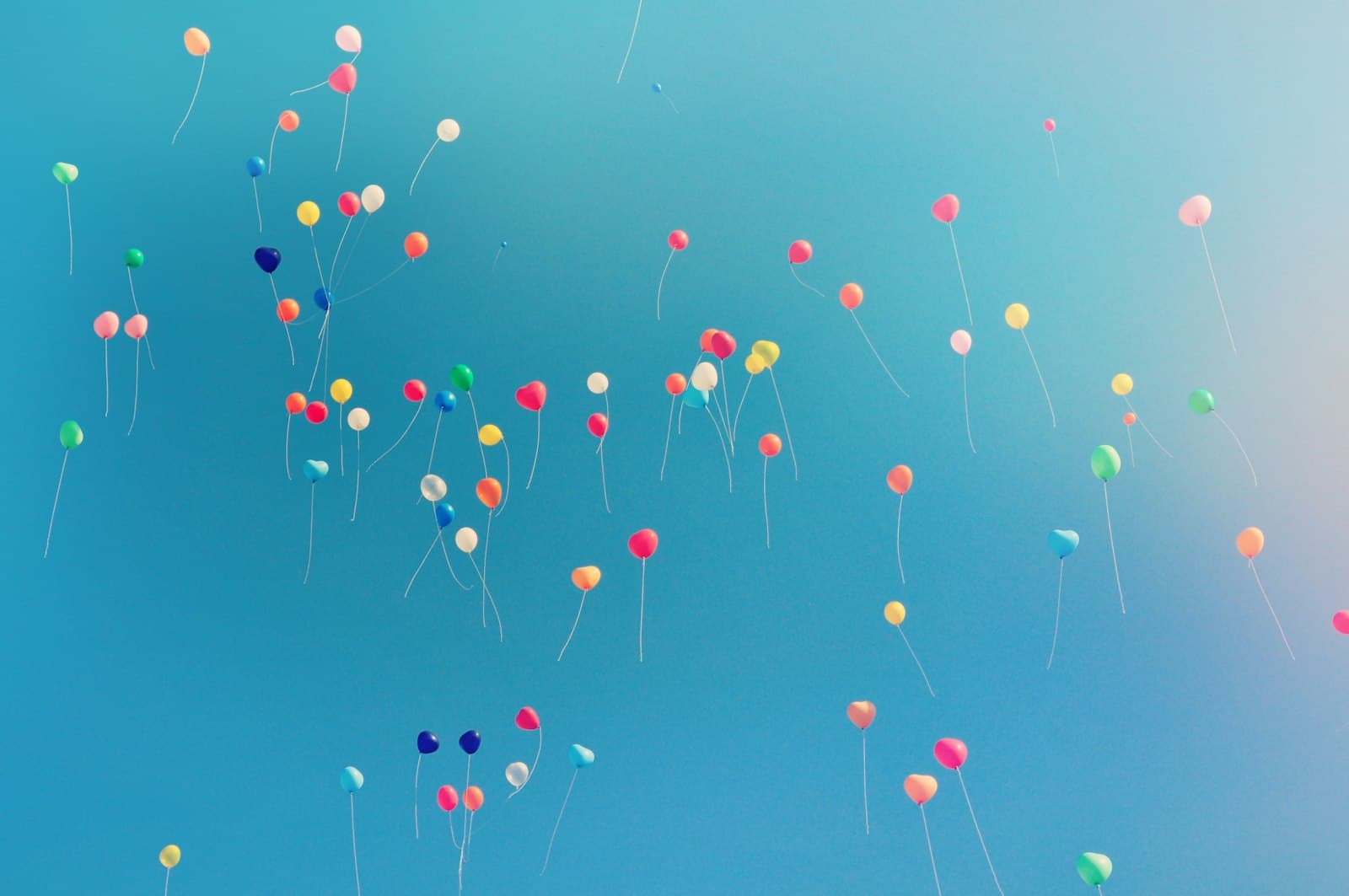 Kleurige ballonnen zweven op tegen een zachtblauwe lucht, een feestelijk beeld bij een bedrijfsjubileum