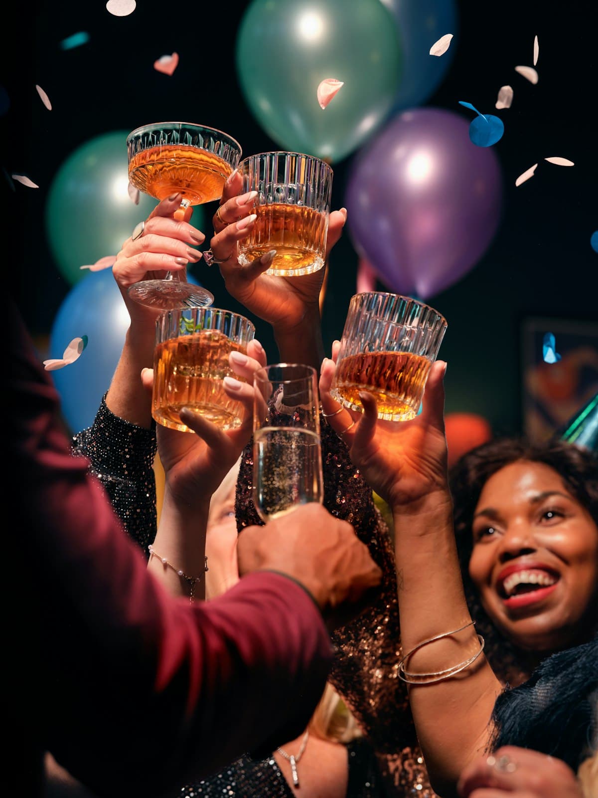Handen heffen het glas onder vallende confetti en kleurige ballonnen tijdens een feestelijke jubileumviering