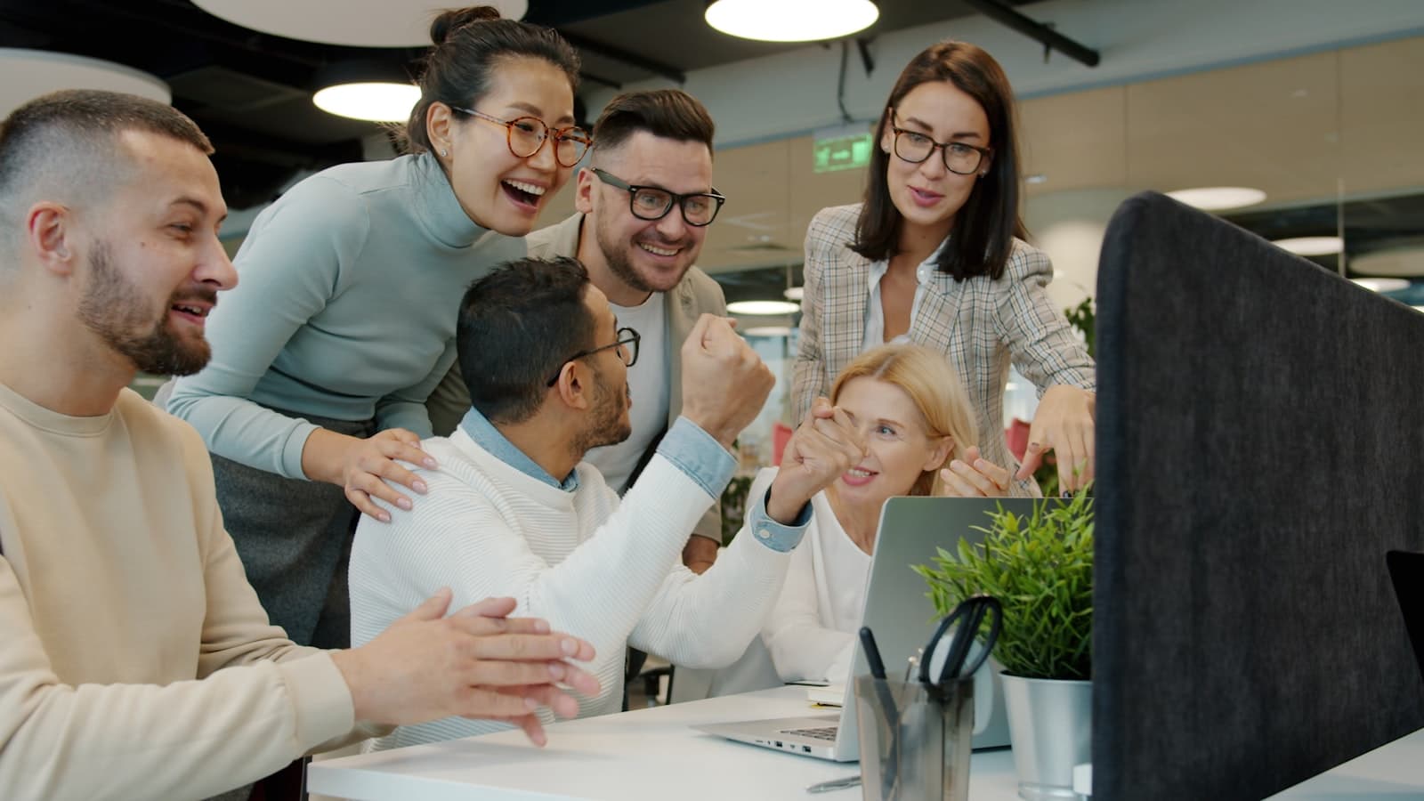 Een divers team collega’s lacht en juicht samen op kantoor tijdens een viering, een warm beeld bij koekjes bestellen voor een bedrijfsjubileum