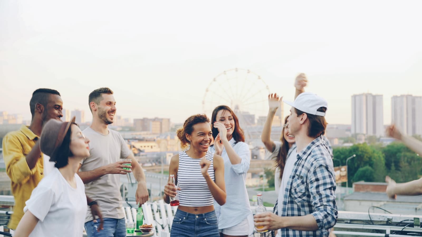 Een diverse groep collega's lacht en danst samen op een dakterras met uitzicht over de stad