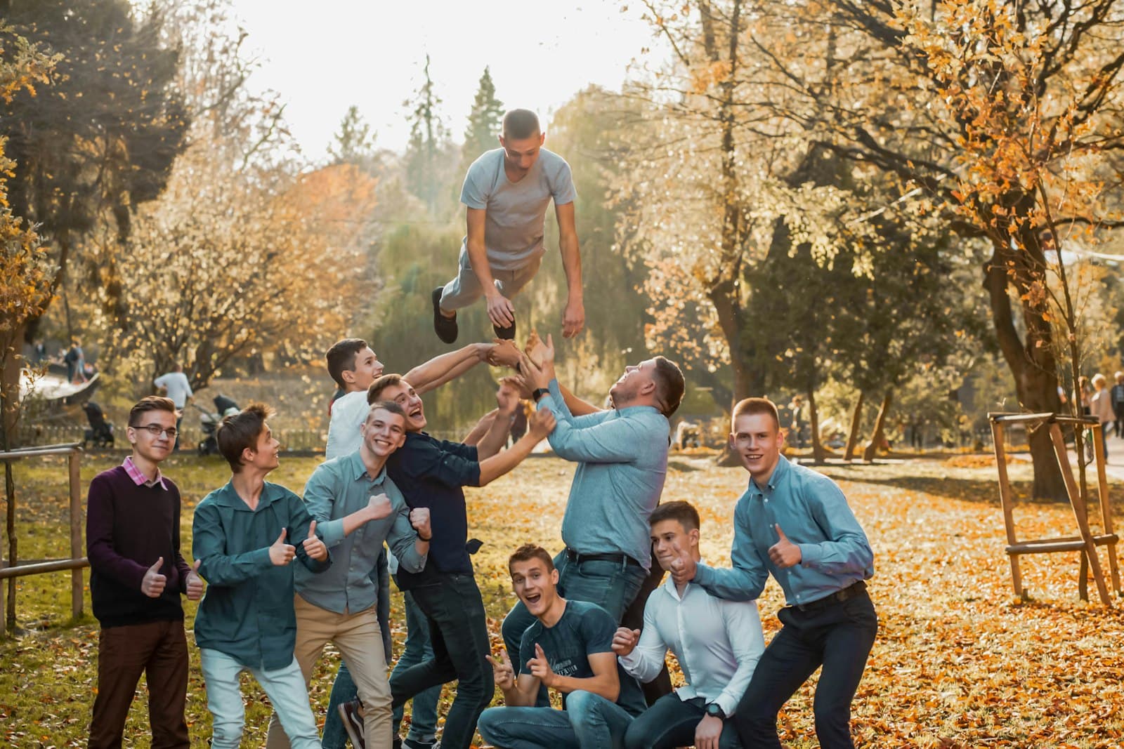 Een team collega's tilt lachend iemand omhoog in een herfstig park tijdens een bedrijfsuitje