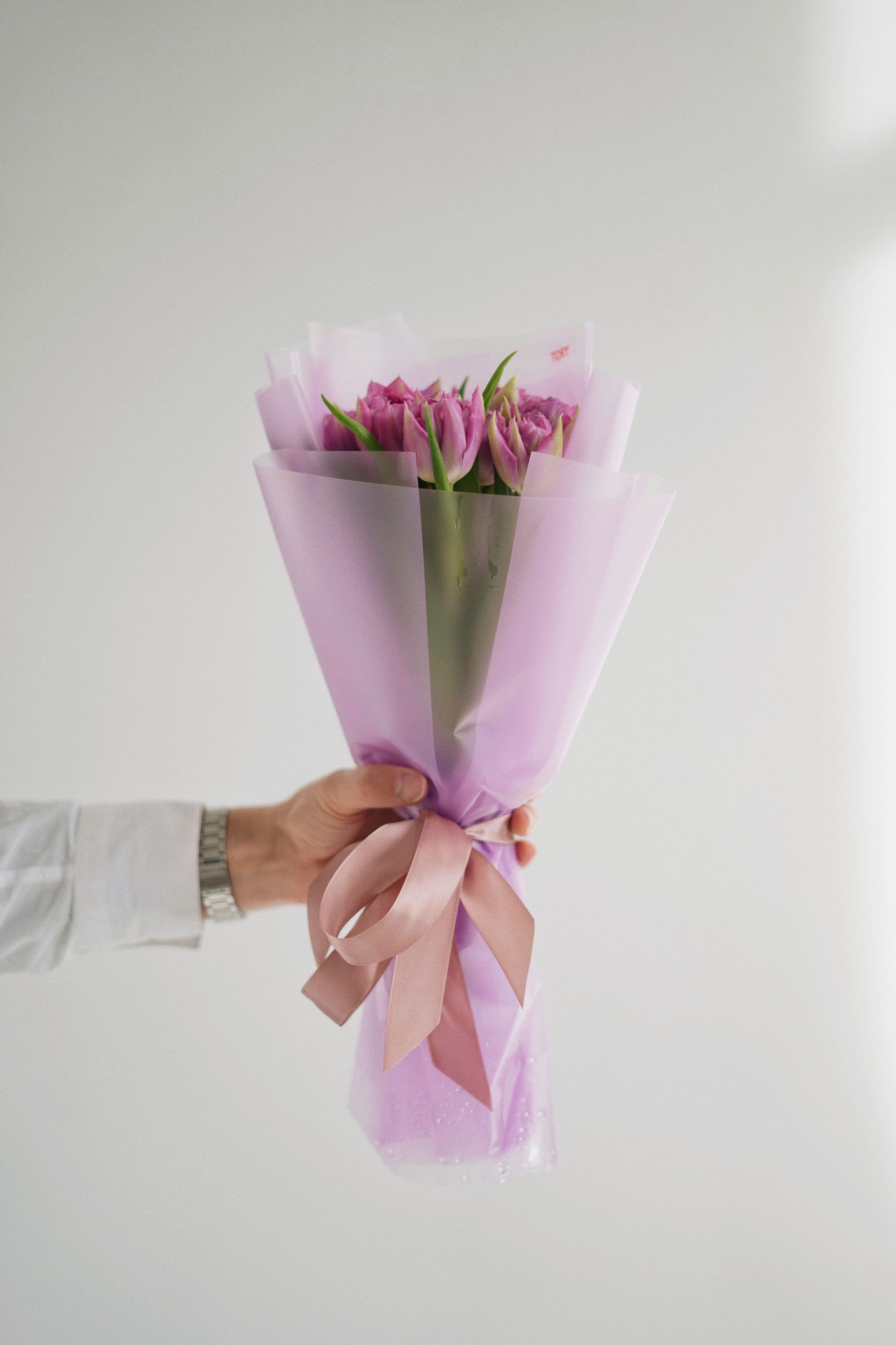 Een hand houdt een fraai ingepakt boeket roze tulpen vast tegen een zachte achtergrond, een warm beeld bij het geven van een attentie