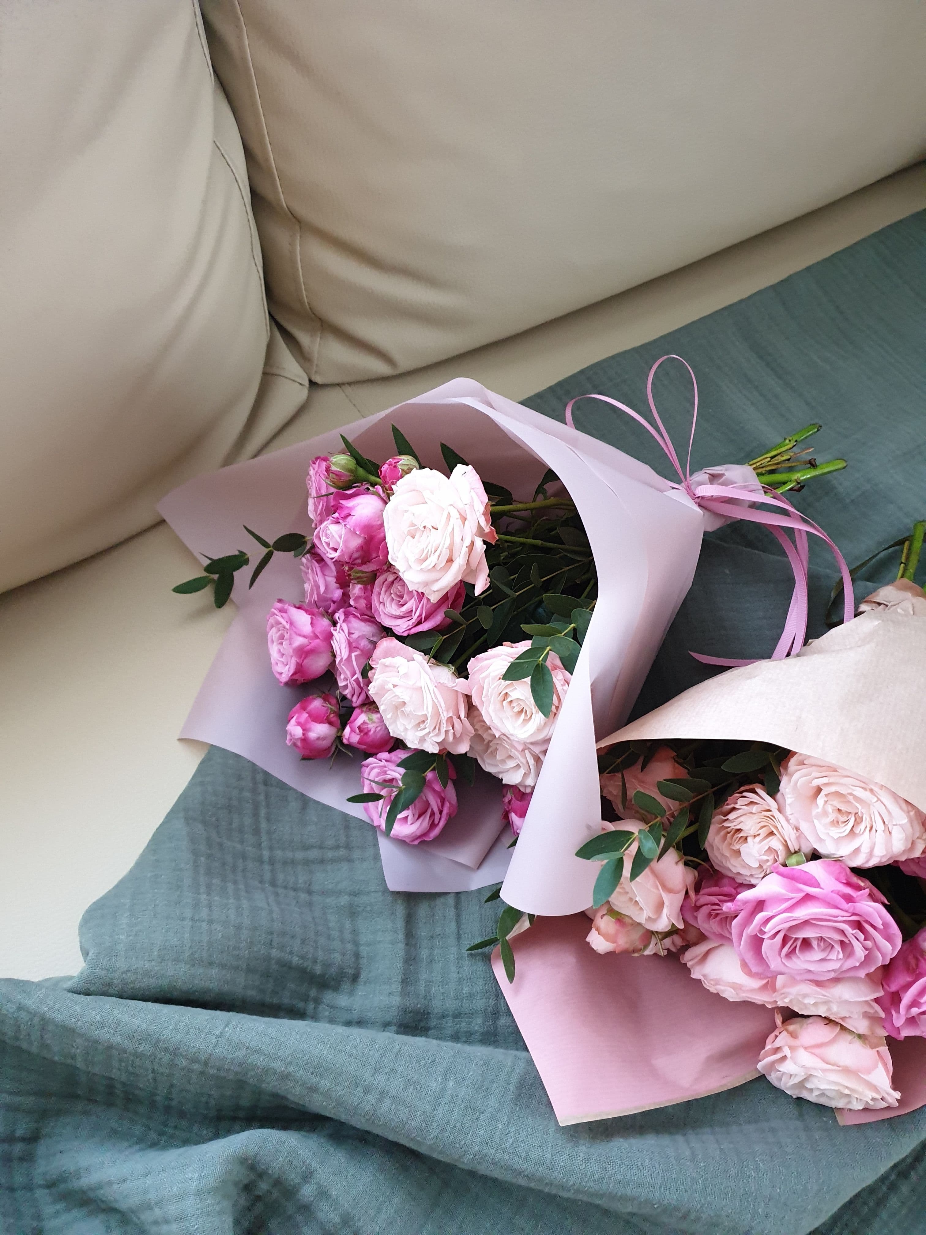 Twee zacht ingepakte boeketten rozen in pastelkleurig papier op een zachte ondergrond, een beeld bij de keuze tussen bloemen en koekjes sturen