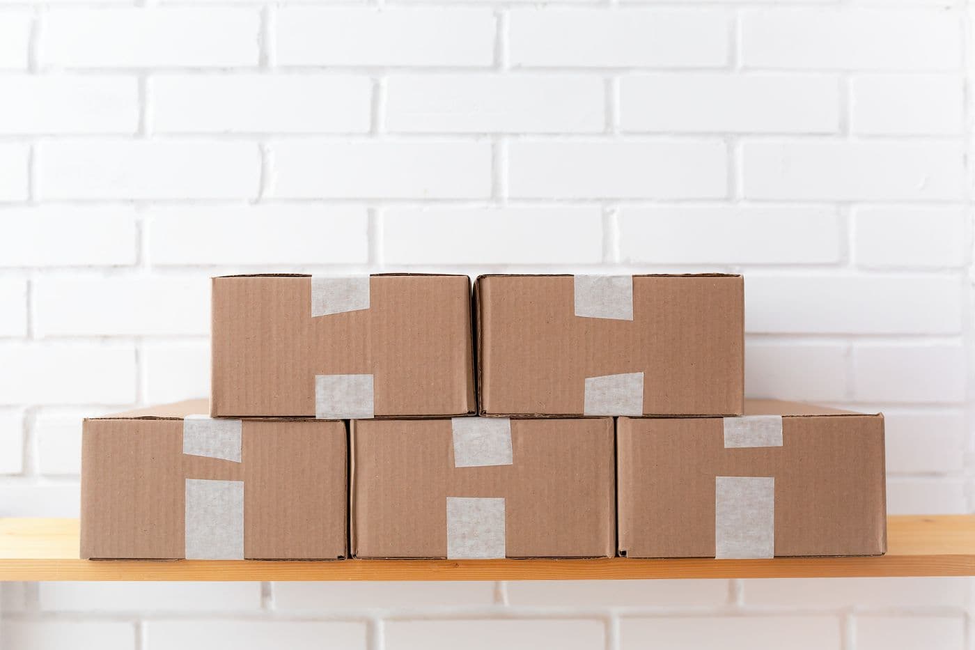 Een nette stapel bruine kartonnen dozen op een houten plank tegen een witte bakstenen muur, klaar om verzonden te worden