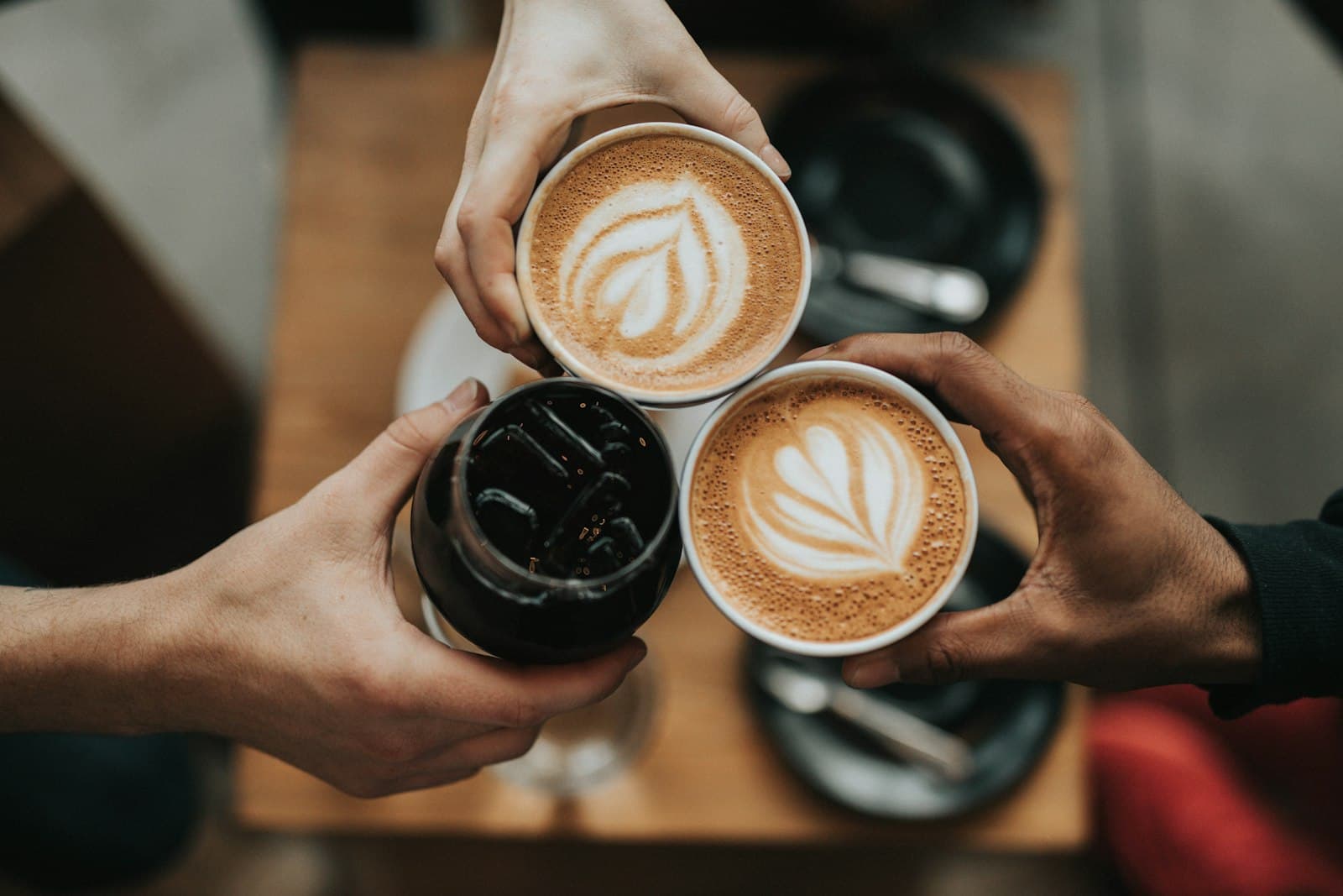Drie mensen proosten met koffiebekers boven een tafel, een sfeerbeeld bij samen koffie drinken op Burendag