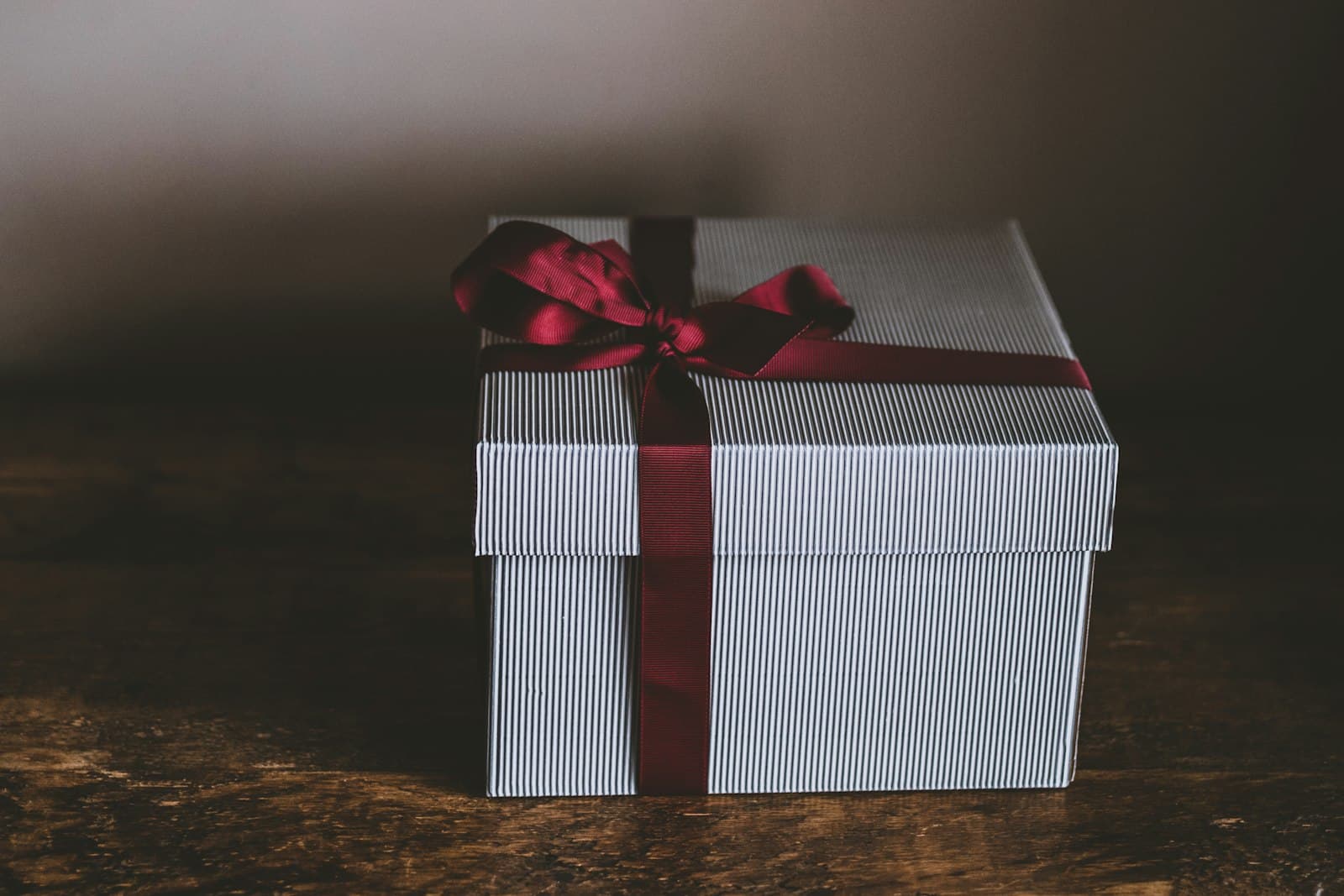 Een elegant ingepakt cadeau met een dieprood lint op een houten tafel, een sfeervol beeld bij een cadeau voor iemand die alles al heeft