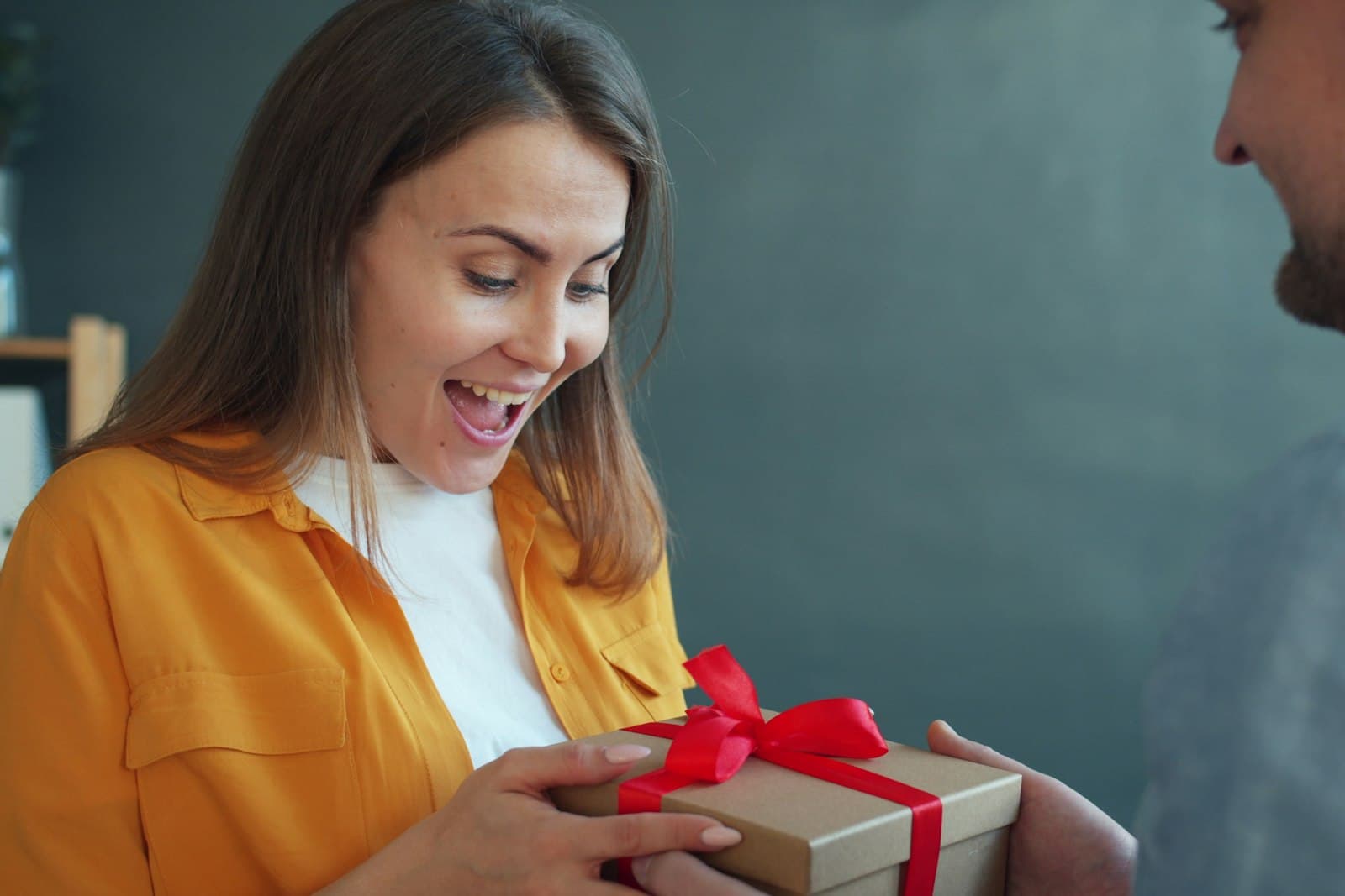 Een vrouw kijkt verrast en blij naar een ingepakt cadeau dat ze in ontvangst neemt, een beeld van de vreugde van een onverwacht cadeau