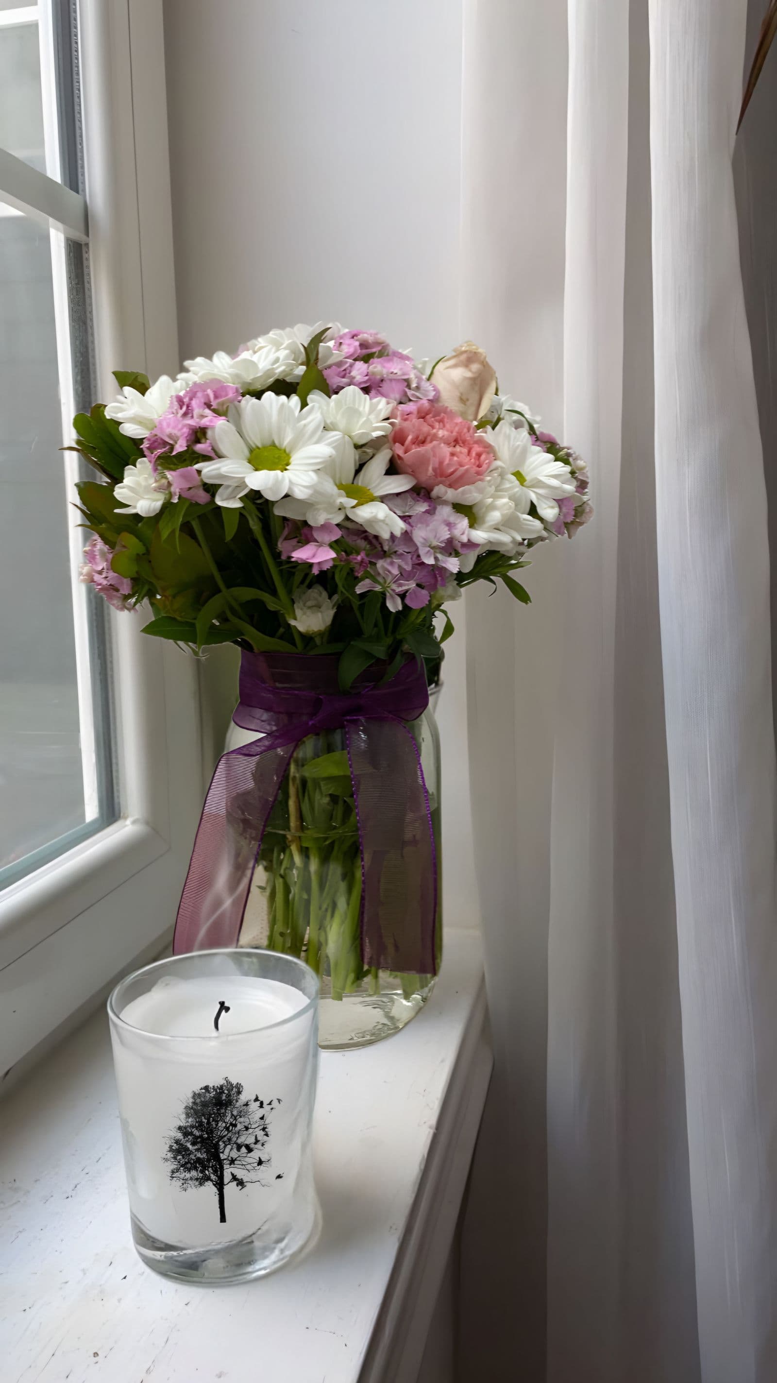 Een boeket witte en roze bloemen met een klein kaarsje op een lichte vensterbank, een zacht en troostend beeld