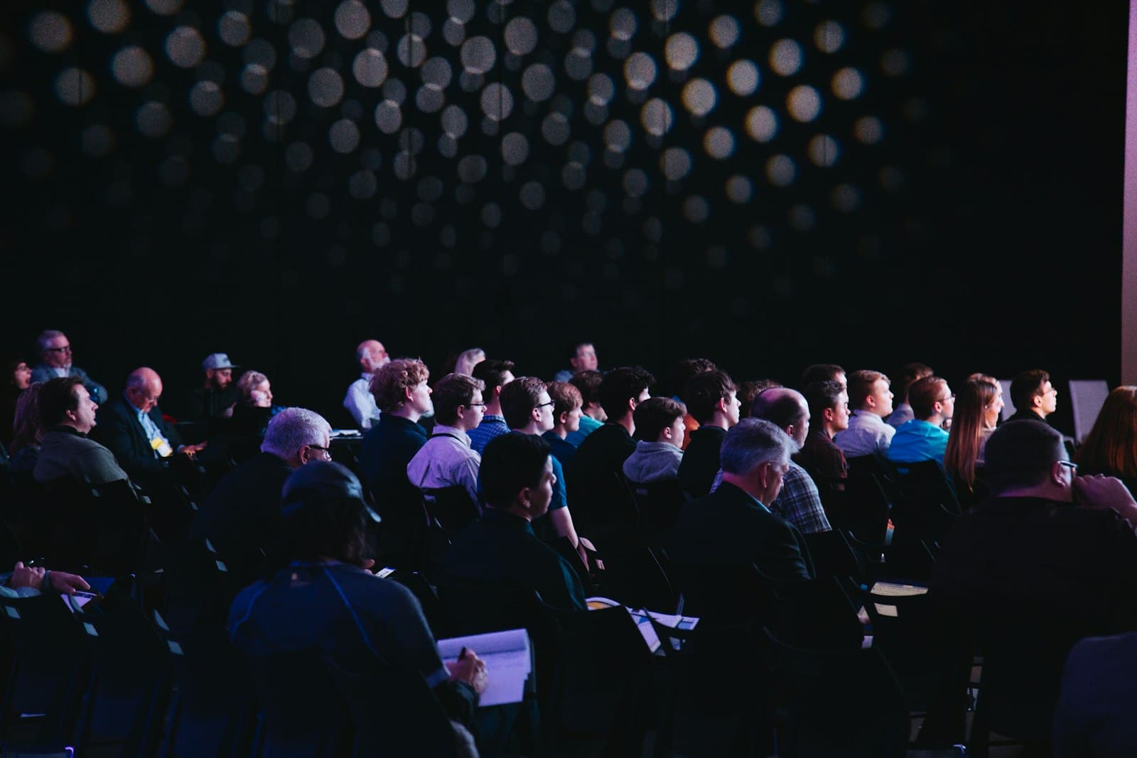 Een aandachtig publiek zit in een zaal te luisteren naar een spreker tijdens een congres