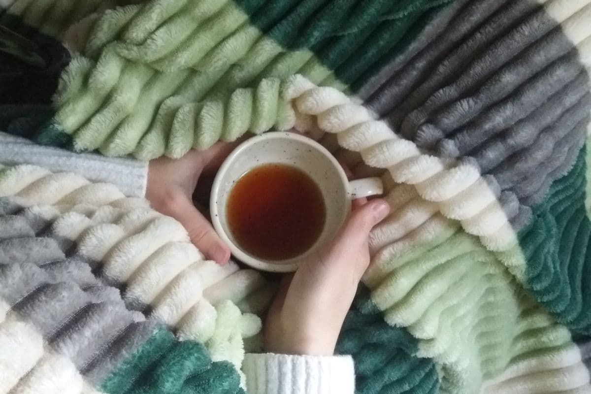 Twee handen omsluiten een kop thee genesteld in een zachte, warme fleece deken tijdens een knusse avond thuis
