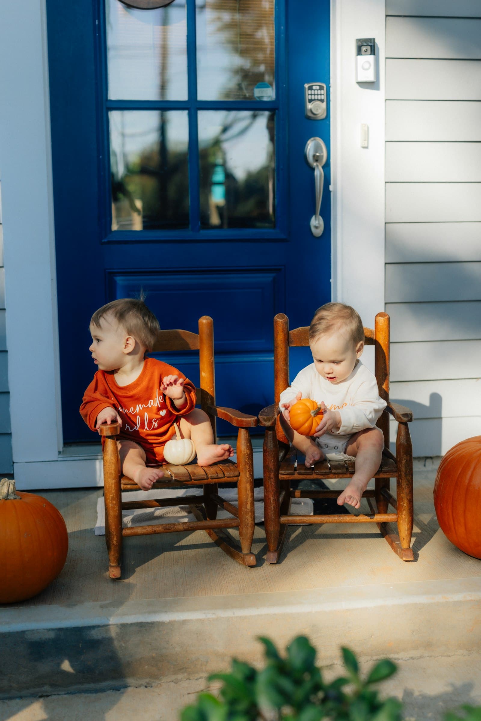 Twee jonge kinderen in herfstkleren zitten op de veranda tussen de pompoenen op een zonnige herfstdag rond Halloween