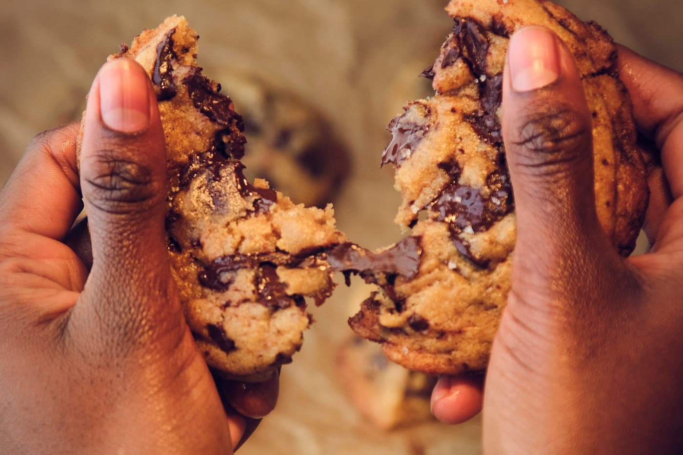 Twee handen breken een chocoladekoekje open, met smeltende pure chocolade tussen de stukken