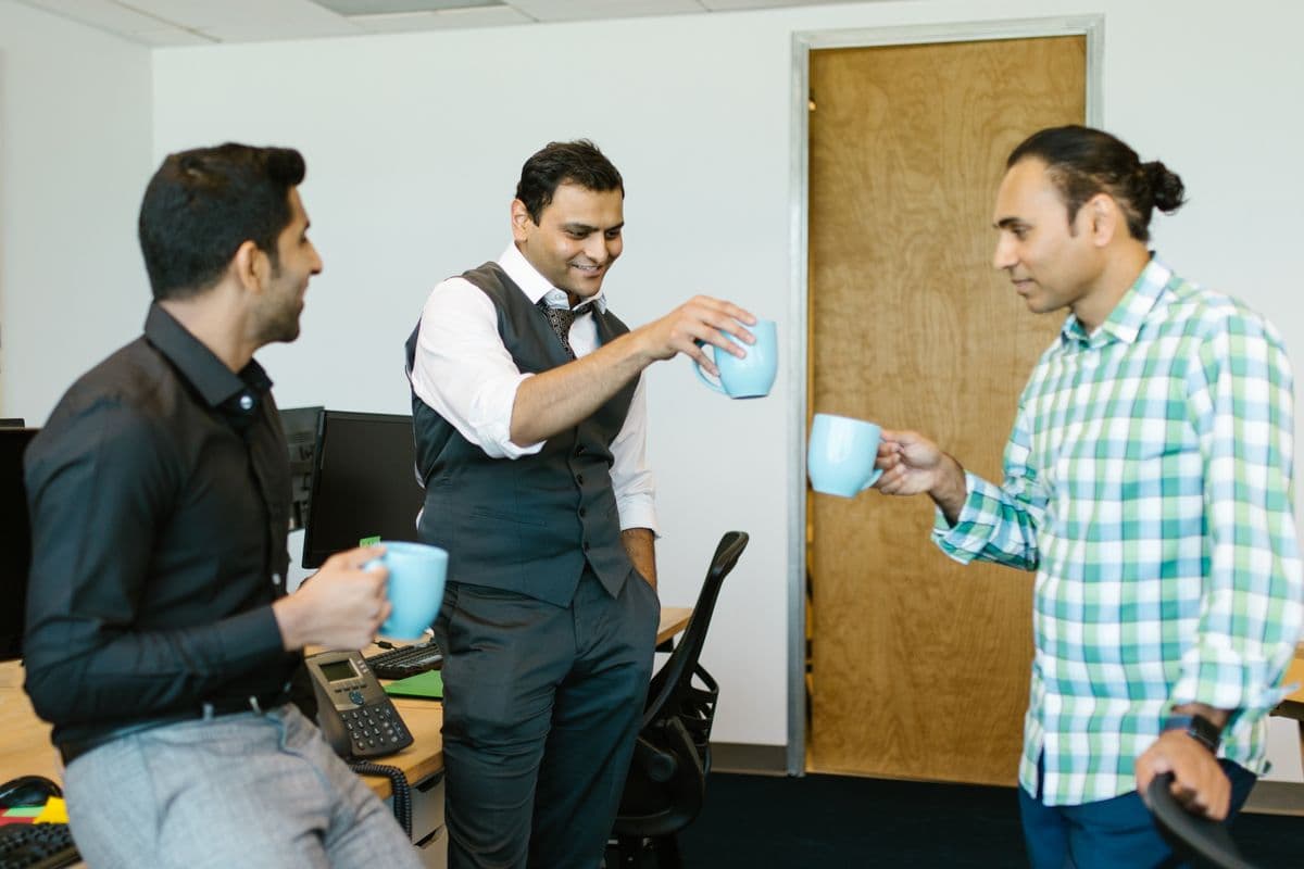 Drie collega's lachen ontspannen samen met een kop koffie in de hand tijdens een pauze op een heidag