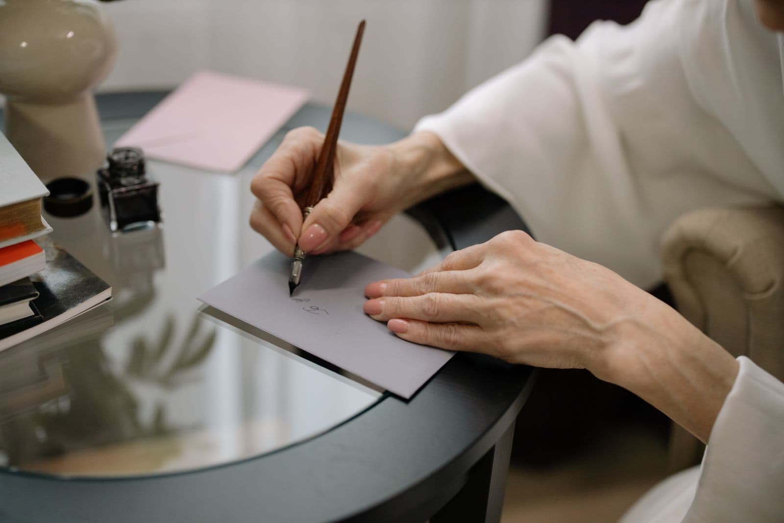 Handen schrijven met een vulpen een kaartje aan een tafel, klaar om mee te sturen met een doos koekjes