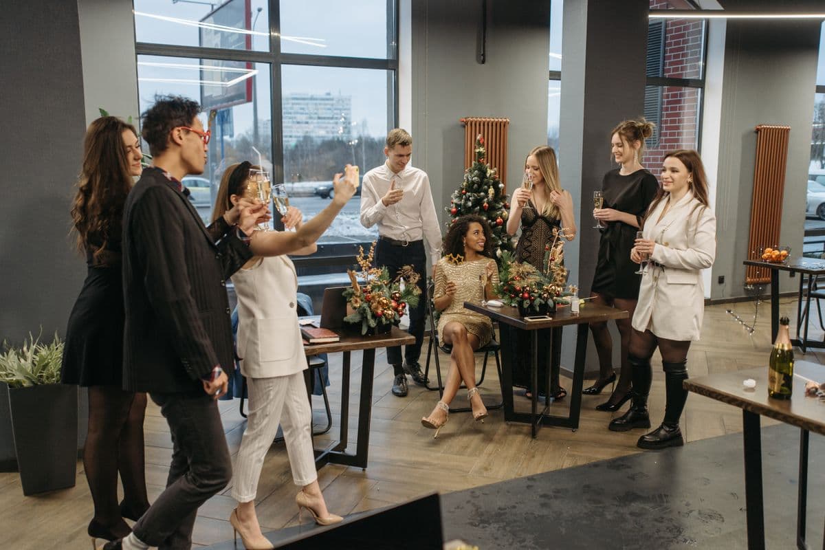 Collega's proosten lachend met glazen omhoog tijdens een feestelijke jaarafsluiting op kantoor met een kerstboom op de achtergrond