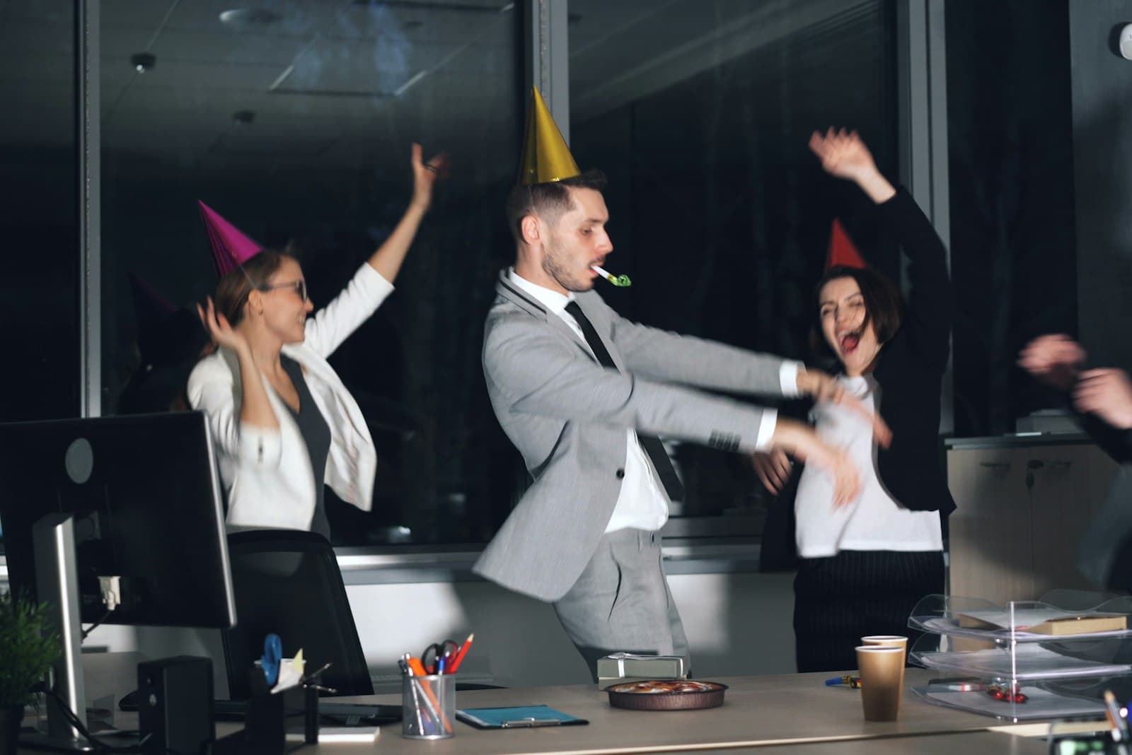 Collega's met feesthoedjes juichen en vieren samen achter een bureau op kantoor, een vrolijk beeld bij jarig op je werk trakteren