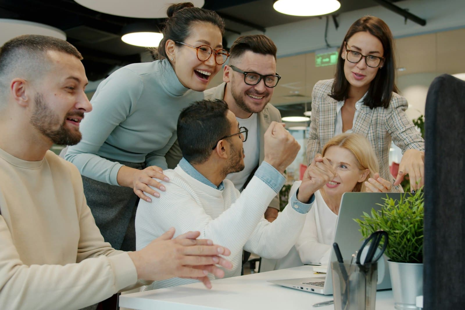 Een diverse groep collega's lacht en viert samen achter een laptop op kantoor, een warm beeld bij trakteren op je werk