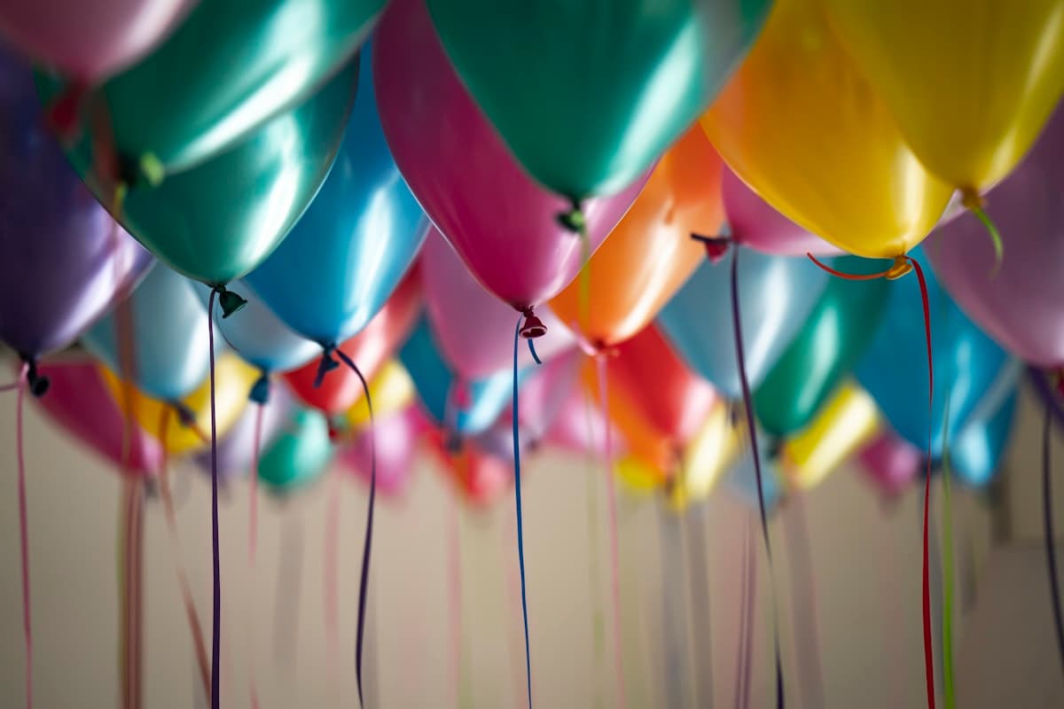 Kleurige ballonnen zweven tegen het plafond met linten die naar beneden hangen, passend bij de feestelijke sfeer van een jubileum