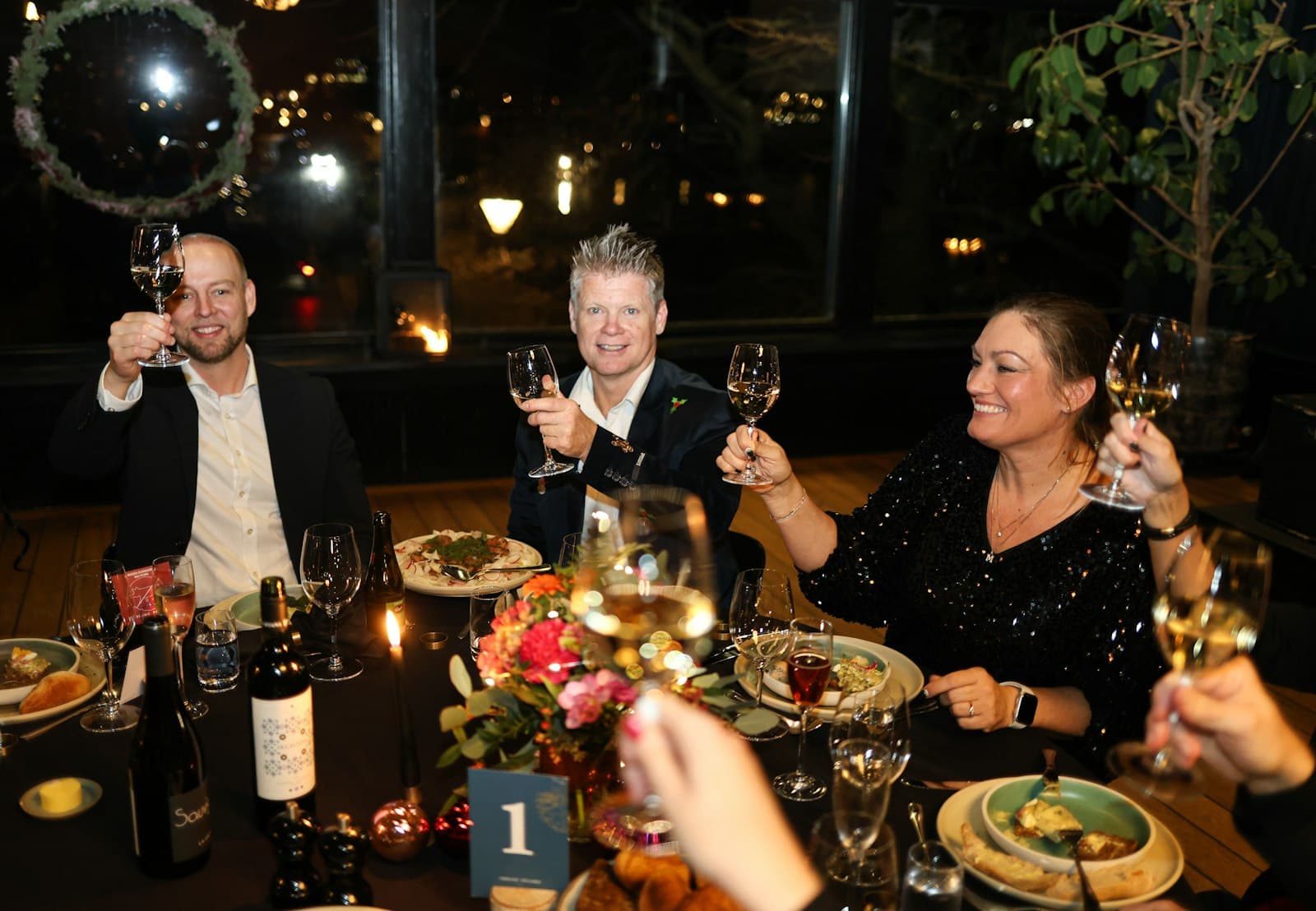 Collega's heffen het glas tijdens een sfeervolle kerstborrel aan een feestelijk gedekte tafel met kaarslicht