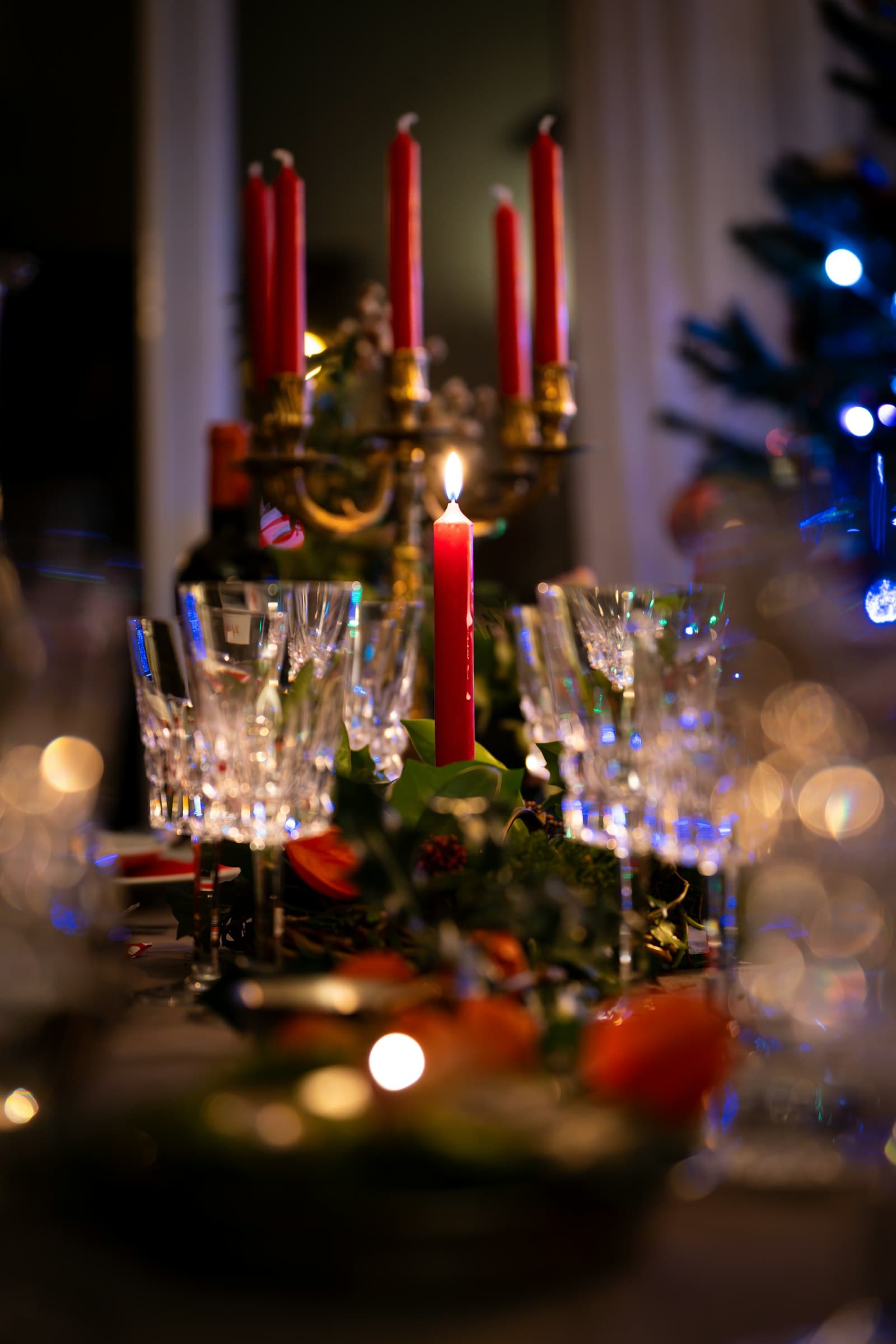 Een feestelijk gedekte tafel met rode kaarsen, kristallen glazen en groen bij een kerstboom, klaar voor een kerstborrel
