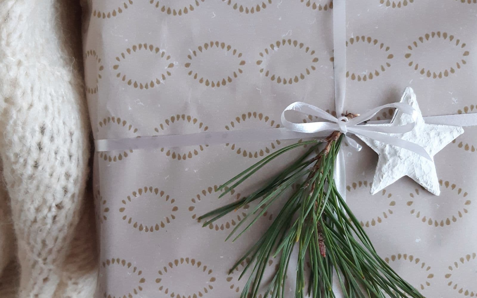 Een met de hand ingepakt kerstcadeau met lint en een dennentakje op een zachte gebreide plaid, een warm en huiselijk beeld bij de kerstdagen
