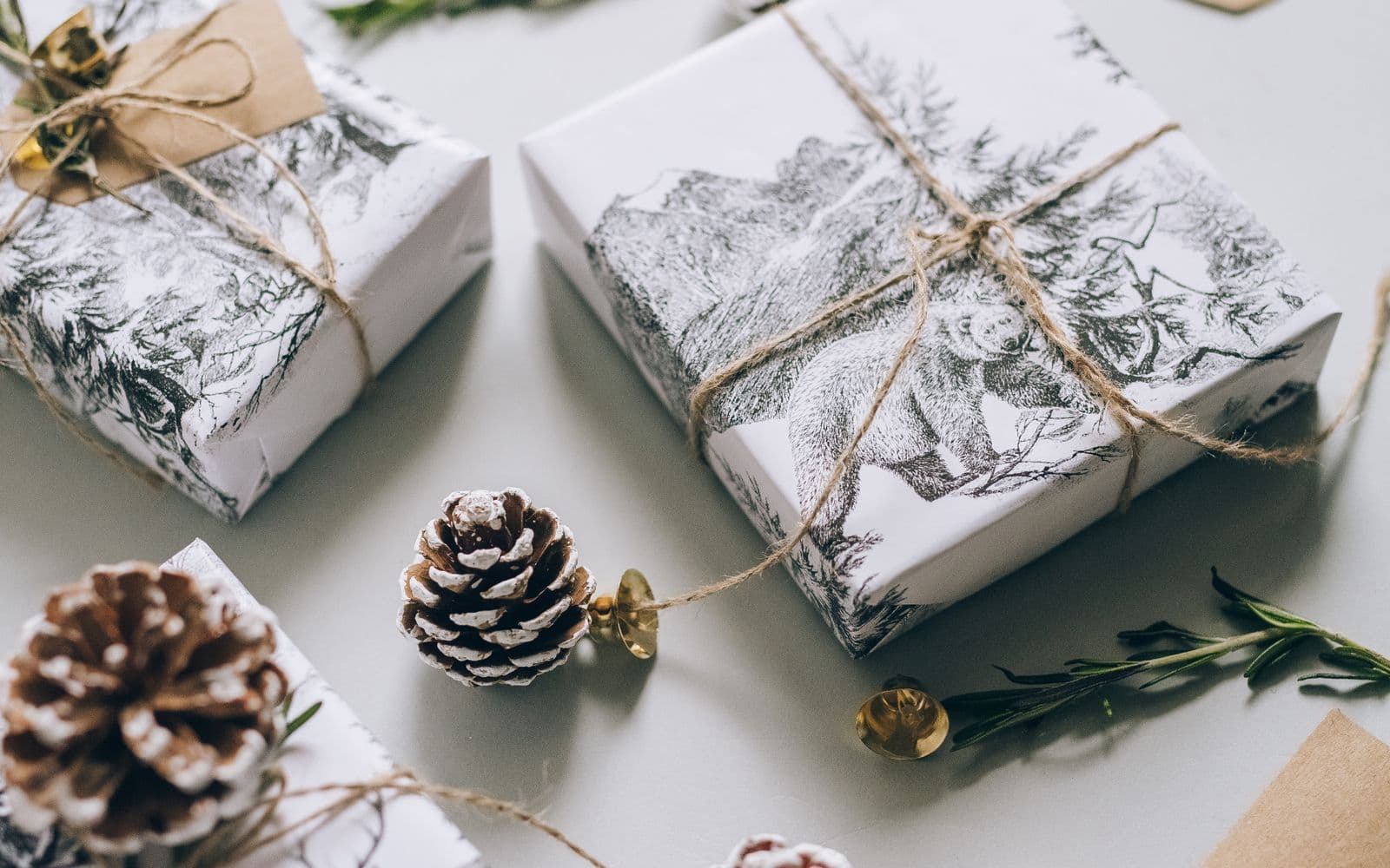 Zorgvuldig ingepakte kerstgeschenken met touw, kraft labels en dennenappels op een lichte tafel, klaar om als zakelijk kerstpakket verstuurd te worden
