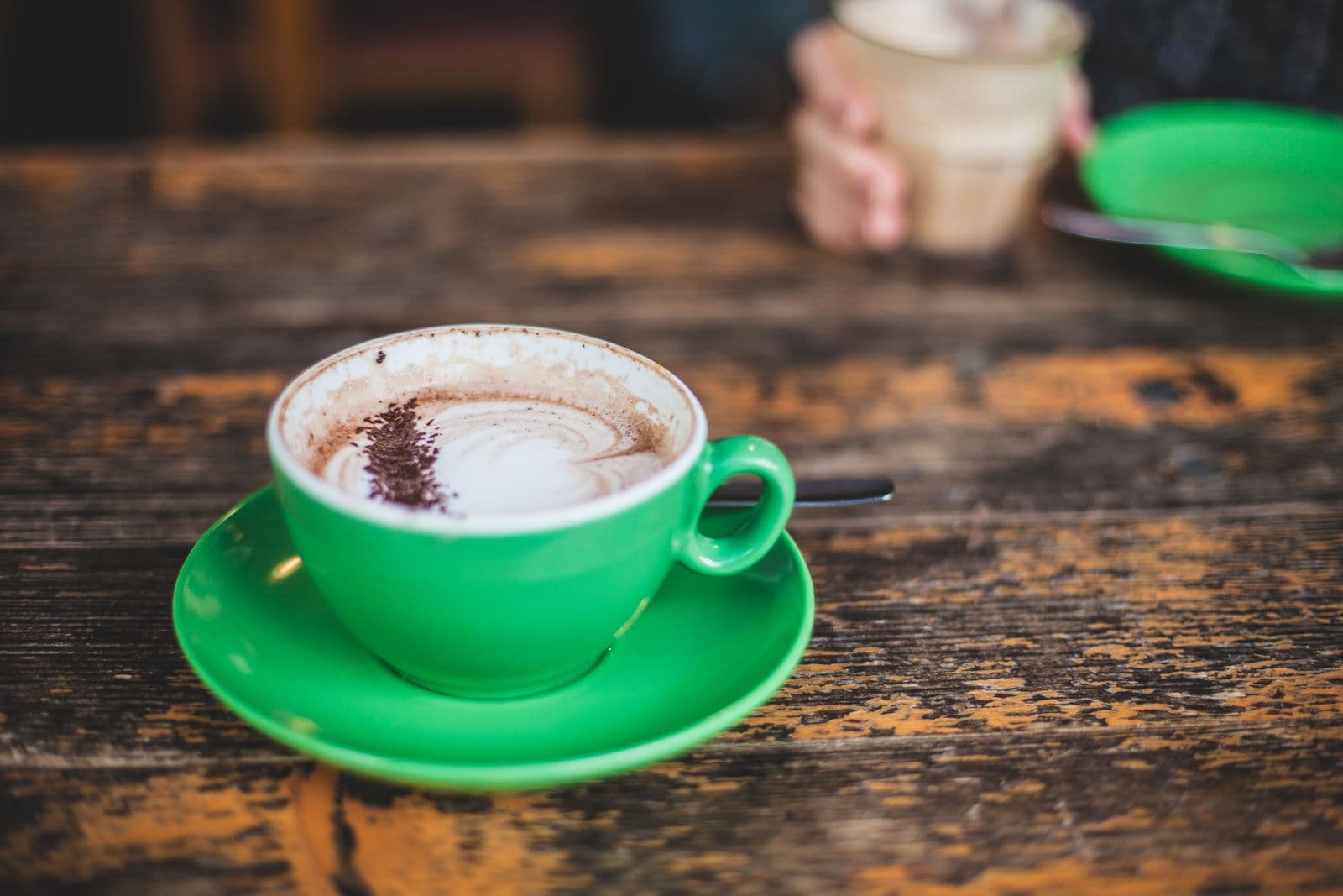 Een groen kopje cappuccino met melkschuim op een houten tafel, een warm beeld bij het moment van een koekje bij de koffie