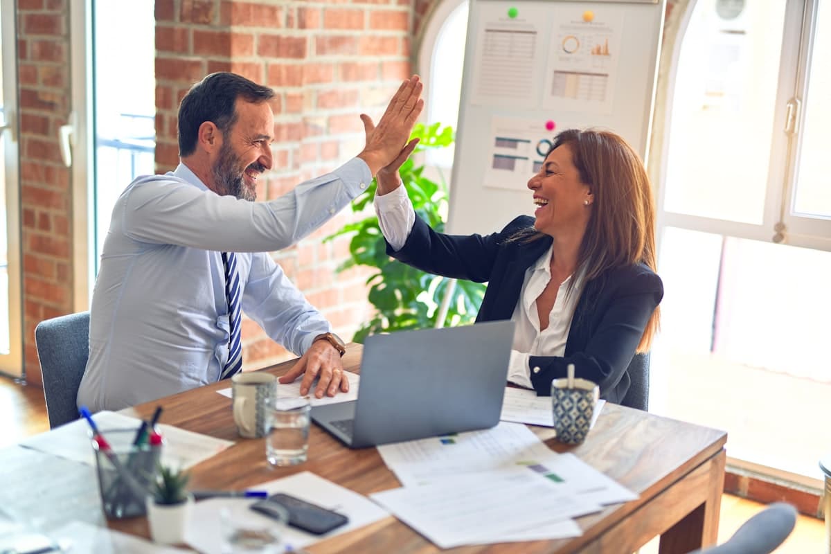 Twee collega's geven elkaar een high five aan een bureau met koffie, een beeld van waardering bij een koekjesabonnement voor kantoor