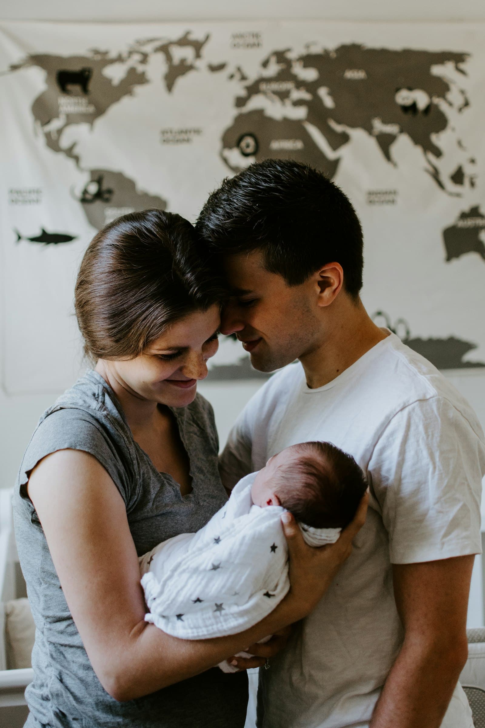 Twee ouders staan met hun voorhoofden tegen elkaar en houden samen hun pasgeboren baby vast thuis