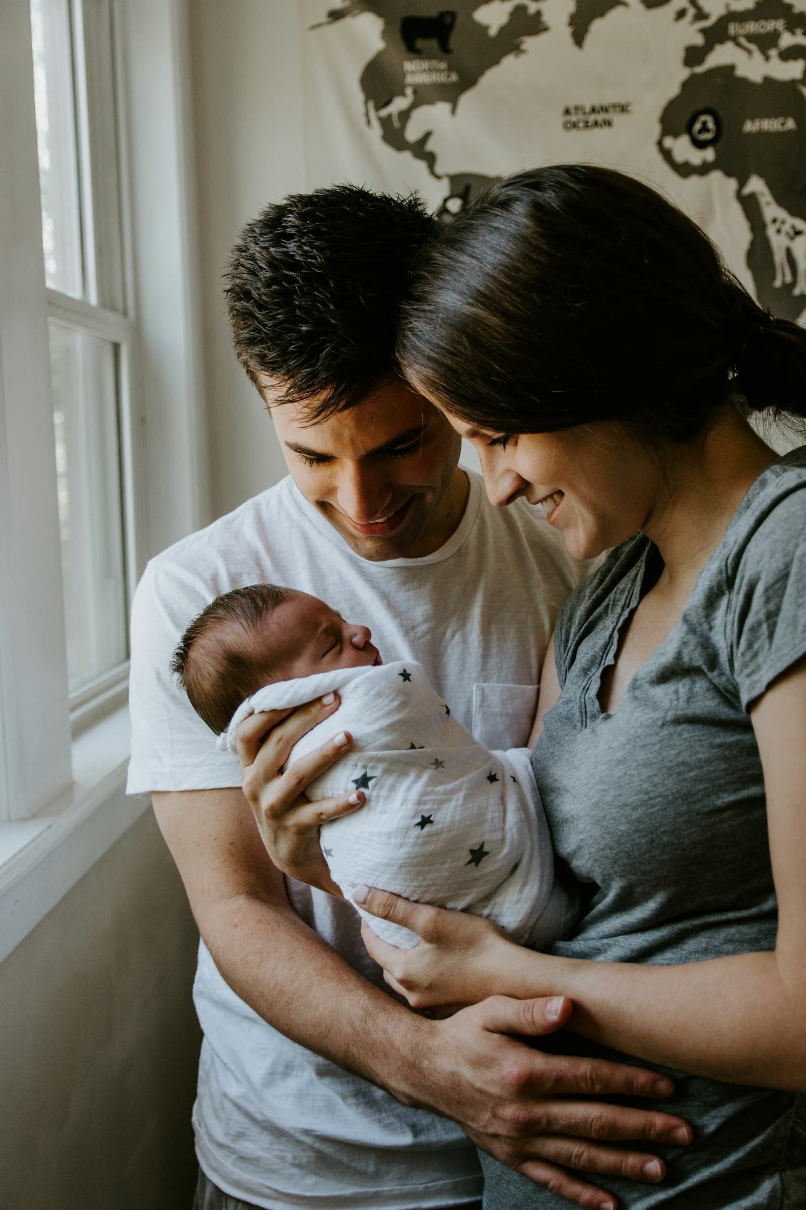 Kersverse ouders kijken glimlachend naar hun pasgeboren baby in een ingebakerd dekentje thuis