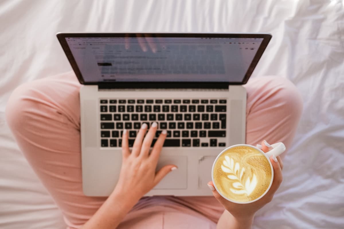 Iemand bestelt op de bank iets online op een laptop met een kop koffie in de hand, een beeld bij koekjes als last-minute cadeau bestellen
