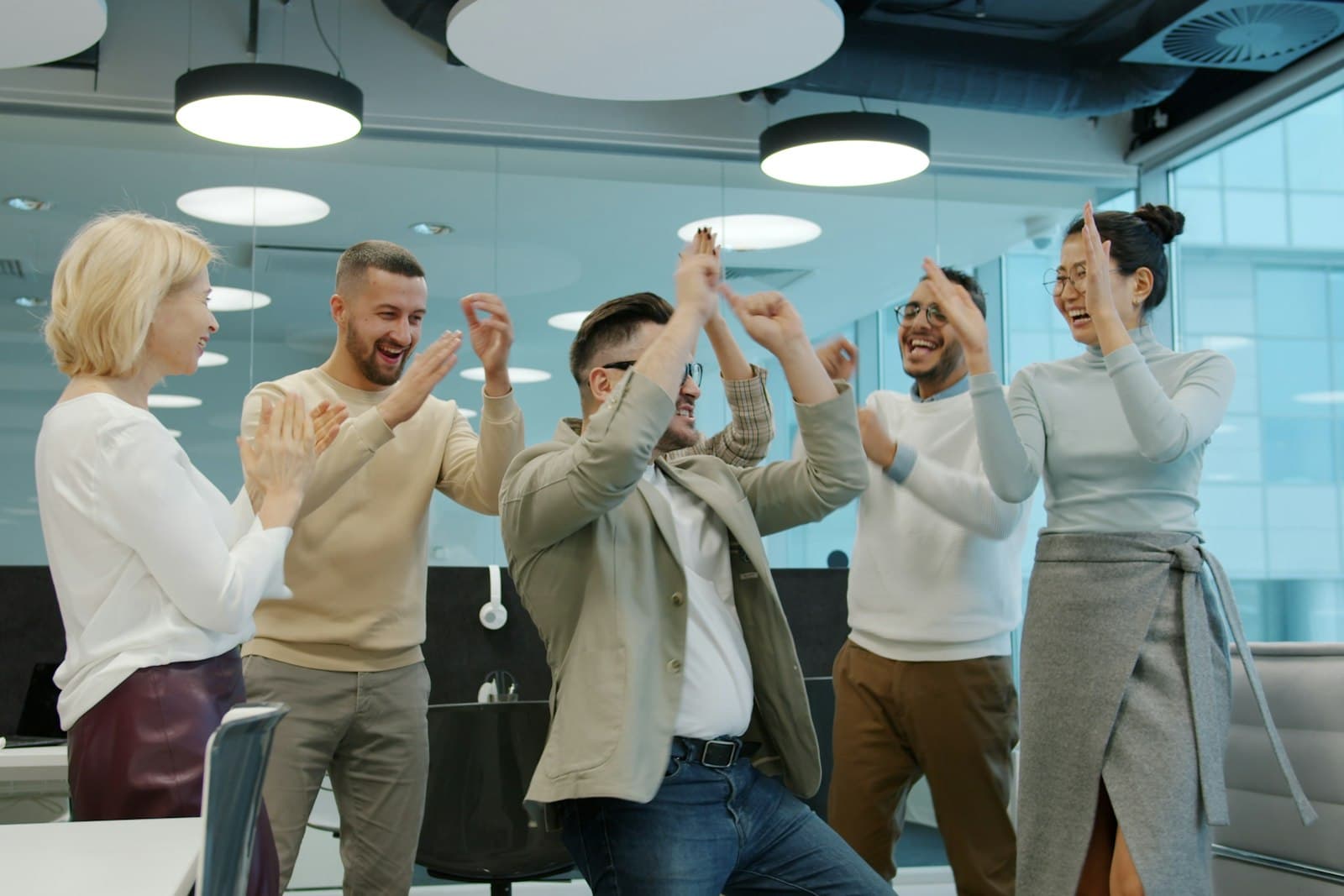 Een divers team viert lachend samen een succes op kantoor met applaus en high fives, een warm beeld bij medewerkerswaardering