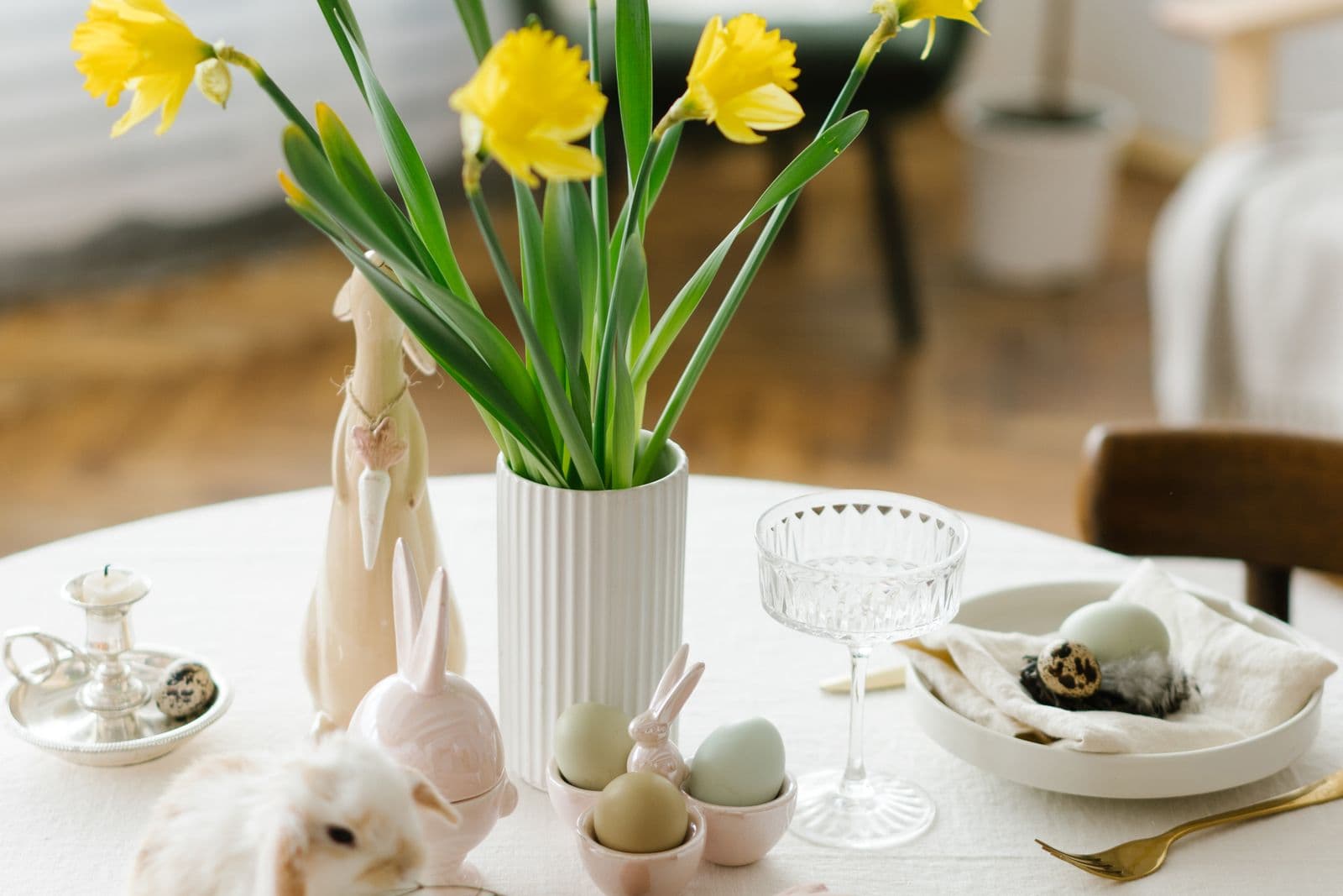 Een lichte paastafel met gele narcissen in een vaas, pastelkleurige eieren en keramieken haasjes, een beeld bij koekjes bestellen met Pasen