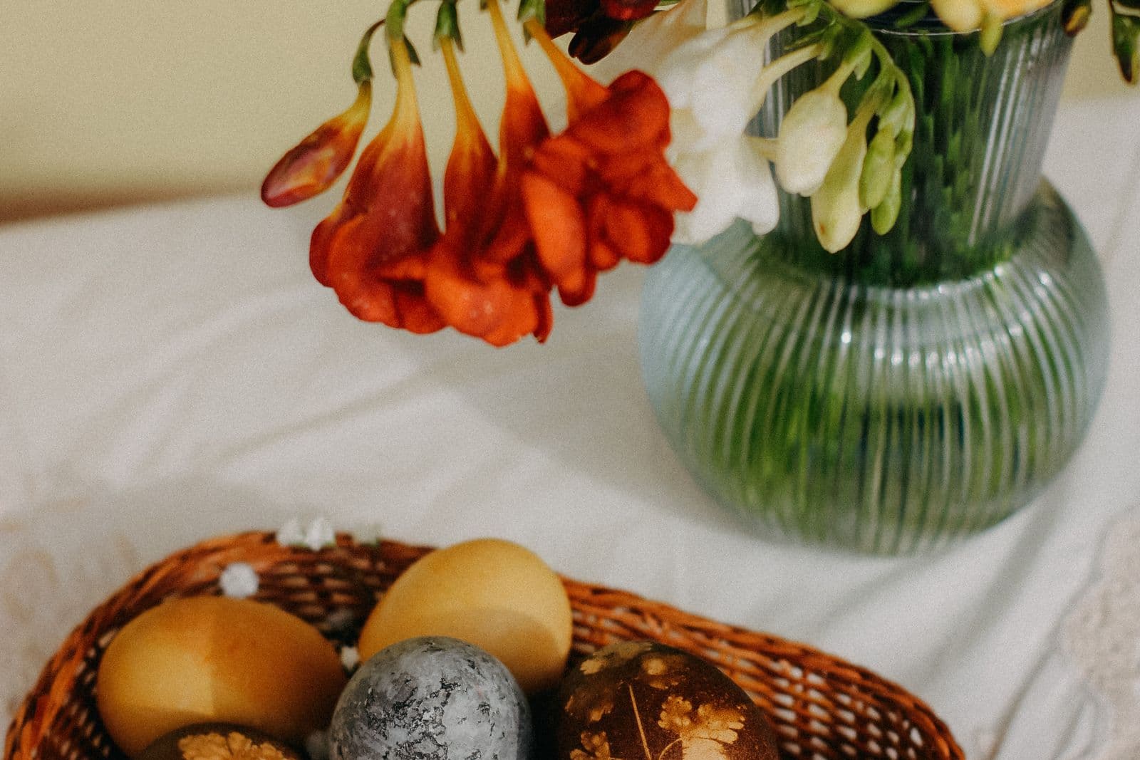 Natuurlijk geverfde paaseieren in een rieten mandje naast een vaas met voorjaarsbloemen op een wit tafelkleed