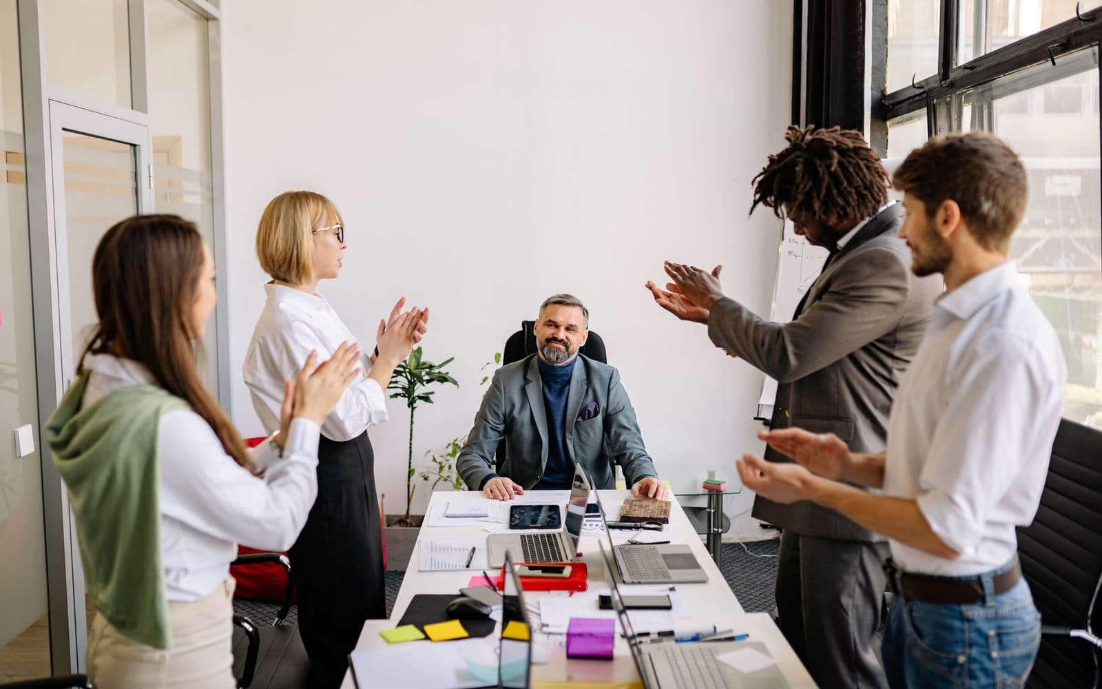 Collega's op kantoor applaudisseren voor een zittende oudere collega tijdens een feestelijk afscheid, een warm beeld bij een pensioenviering