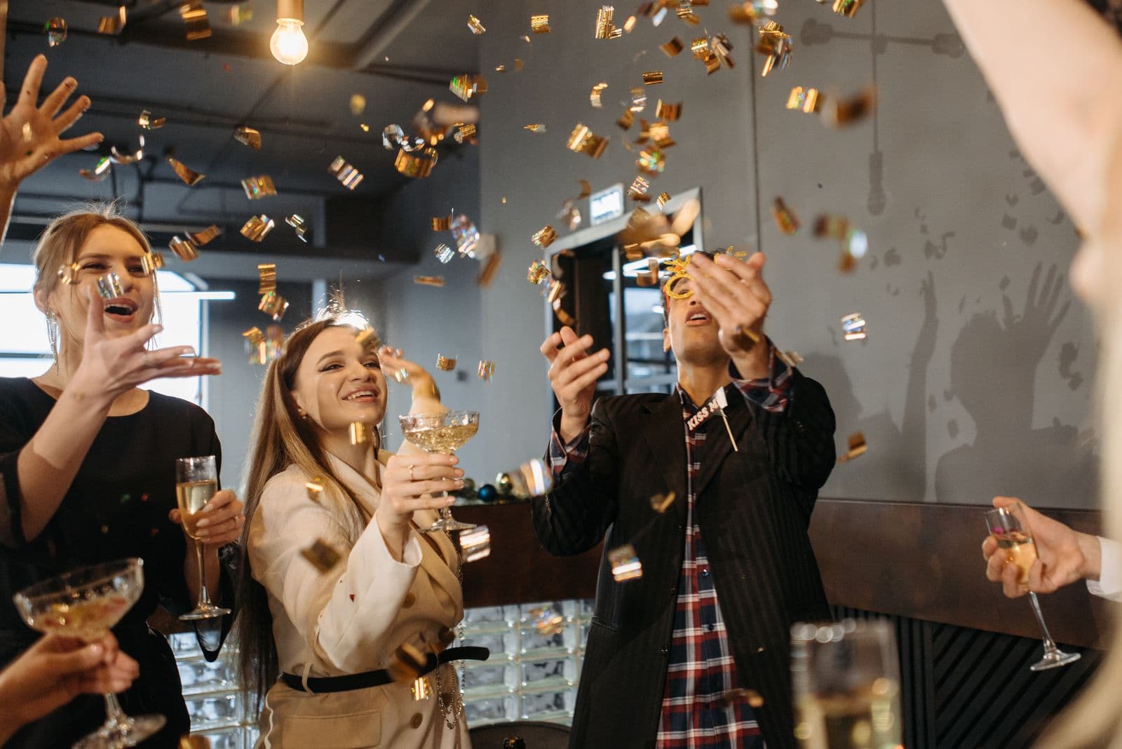 Collega's proosten lachend met een glas en gooien gouden confetti in de lucht tijdens een personeelsfeest