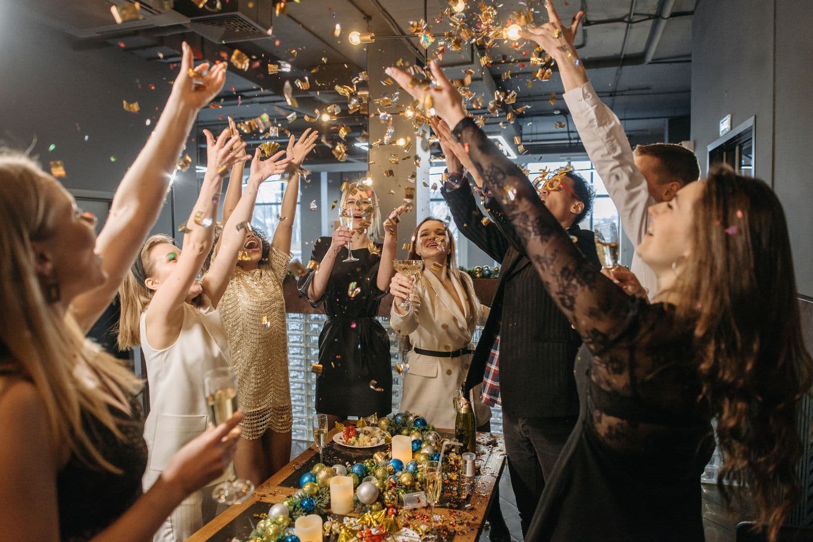 Een groep collega's steekt lachend de armen omhoog terwijl gouden confetti naar beneden dwarrelt op een personeelsfeest