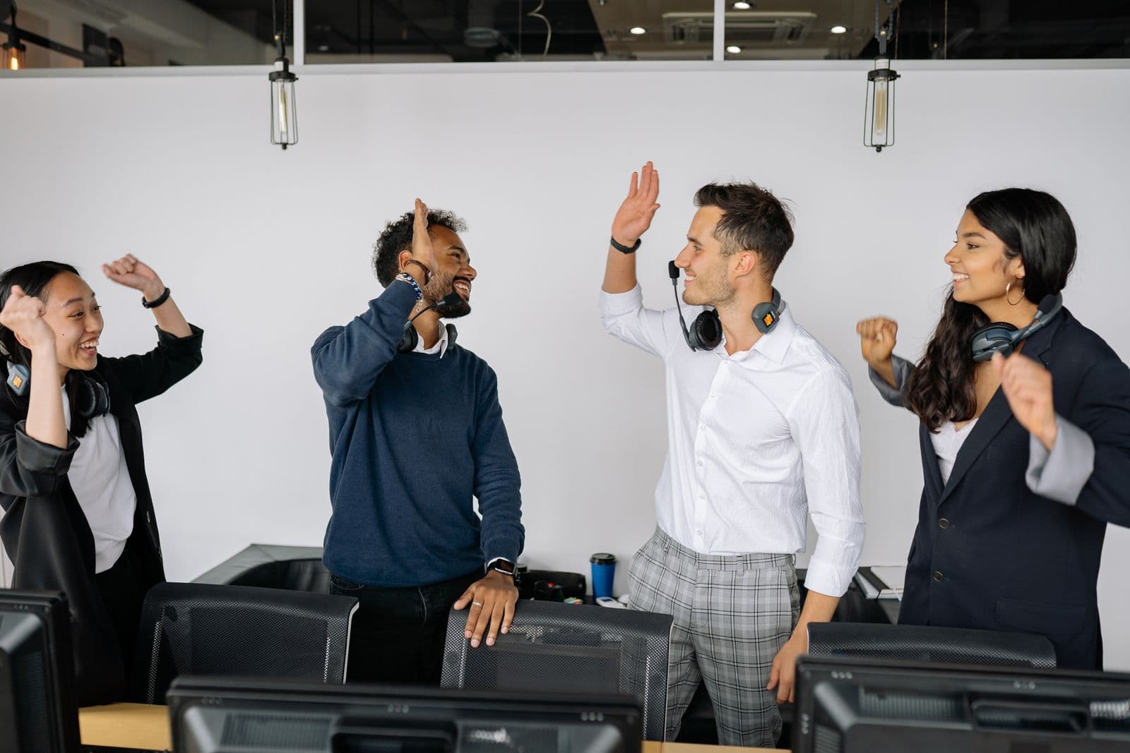 Een divers team van collega's geeft elkaar lachend een high five op kantoor na een succes, een beeld bij het team bedanken na een productlancering