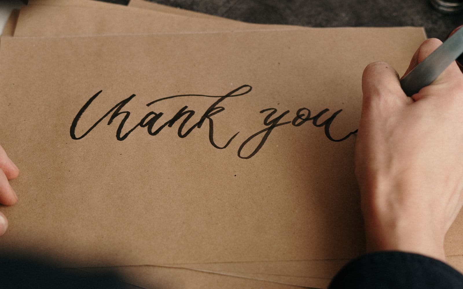 Een hand schrijft met een kalligrafiepen de woorden thank you op kraftpapier, een warm beeld bij een handgeschreven bedankje op Secretaressedag