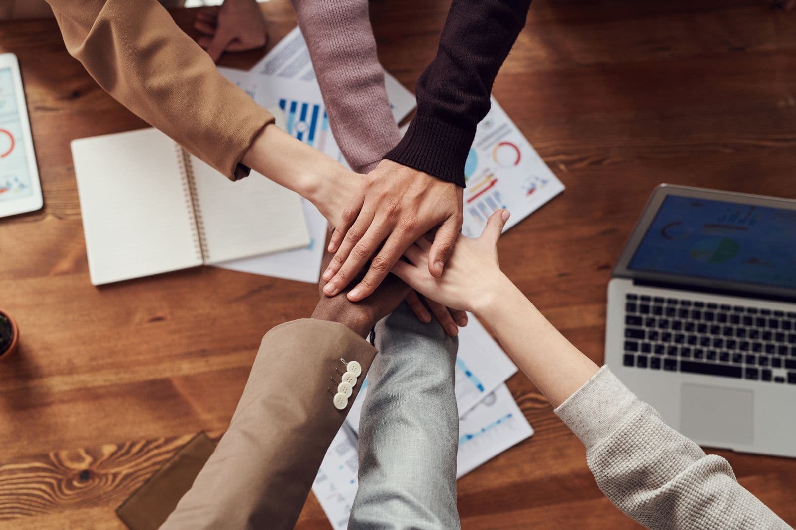 Vier collega’s leggen hun handen op elkaar boven een tafel als teken van samenwerking tijdens een teamdag