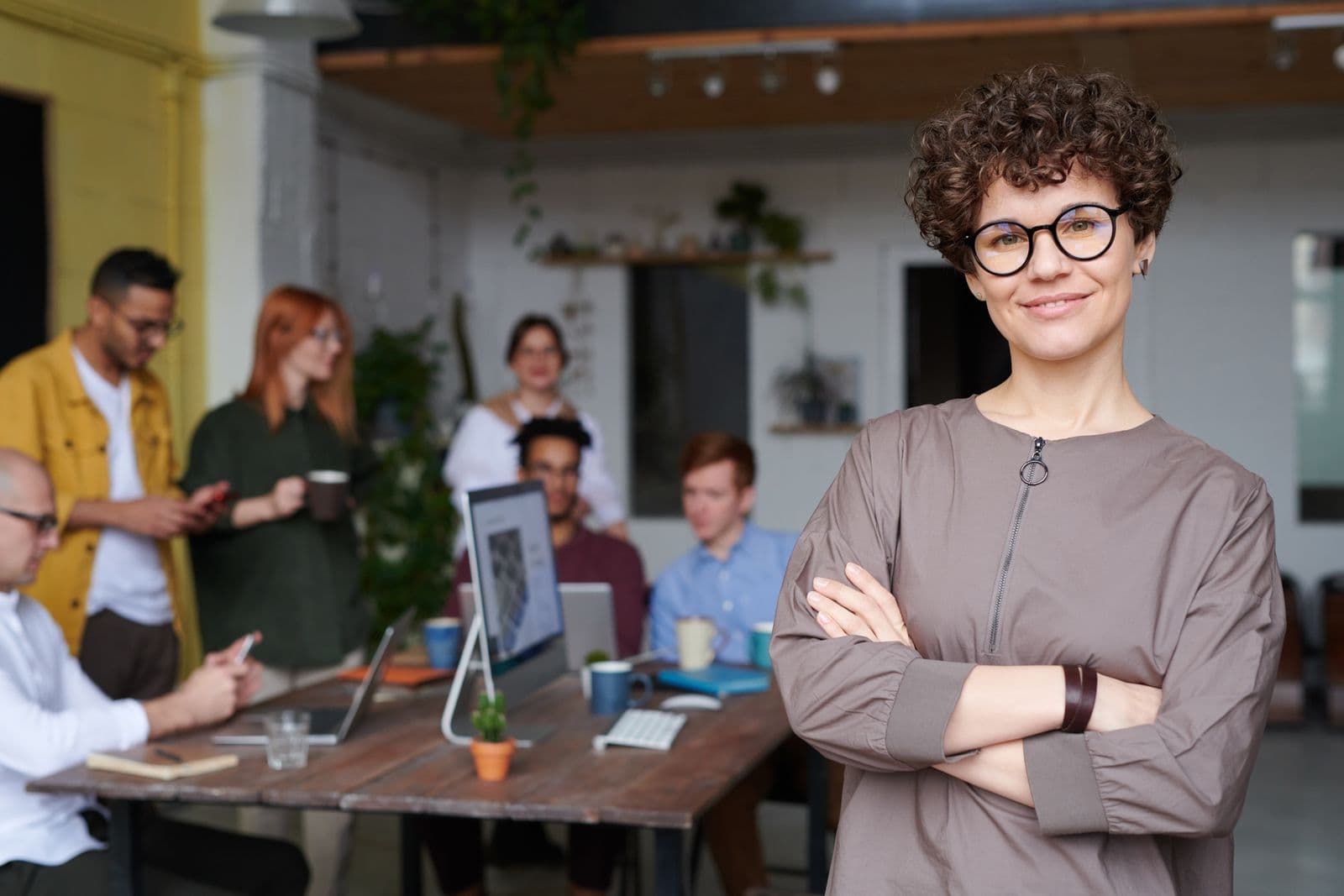 Een lachende collega staat vooraan terwijl haar team ontspannen met een kop koffie overlegt in een lichte werkruimte tijdens een teamdag