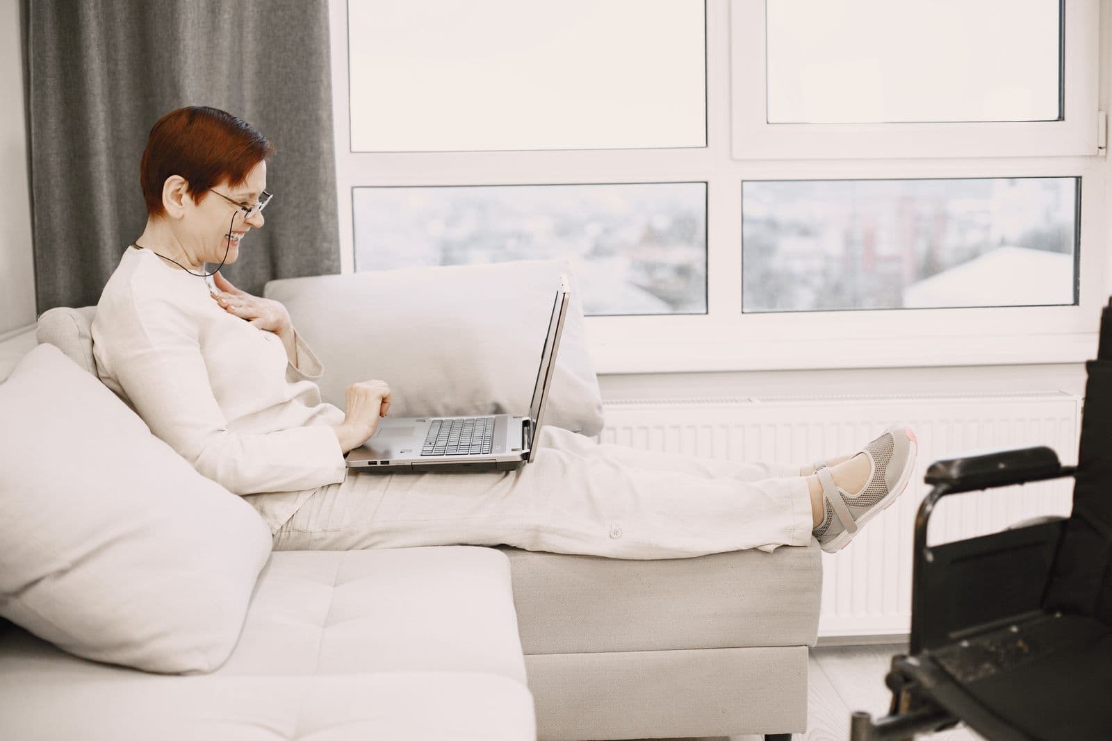 Een collega werkt ontspannen thuis met een laptop op schoot bij het raam, een beeld bij koekjes bestellen voor thuiswerkende collega's