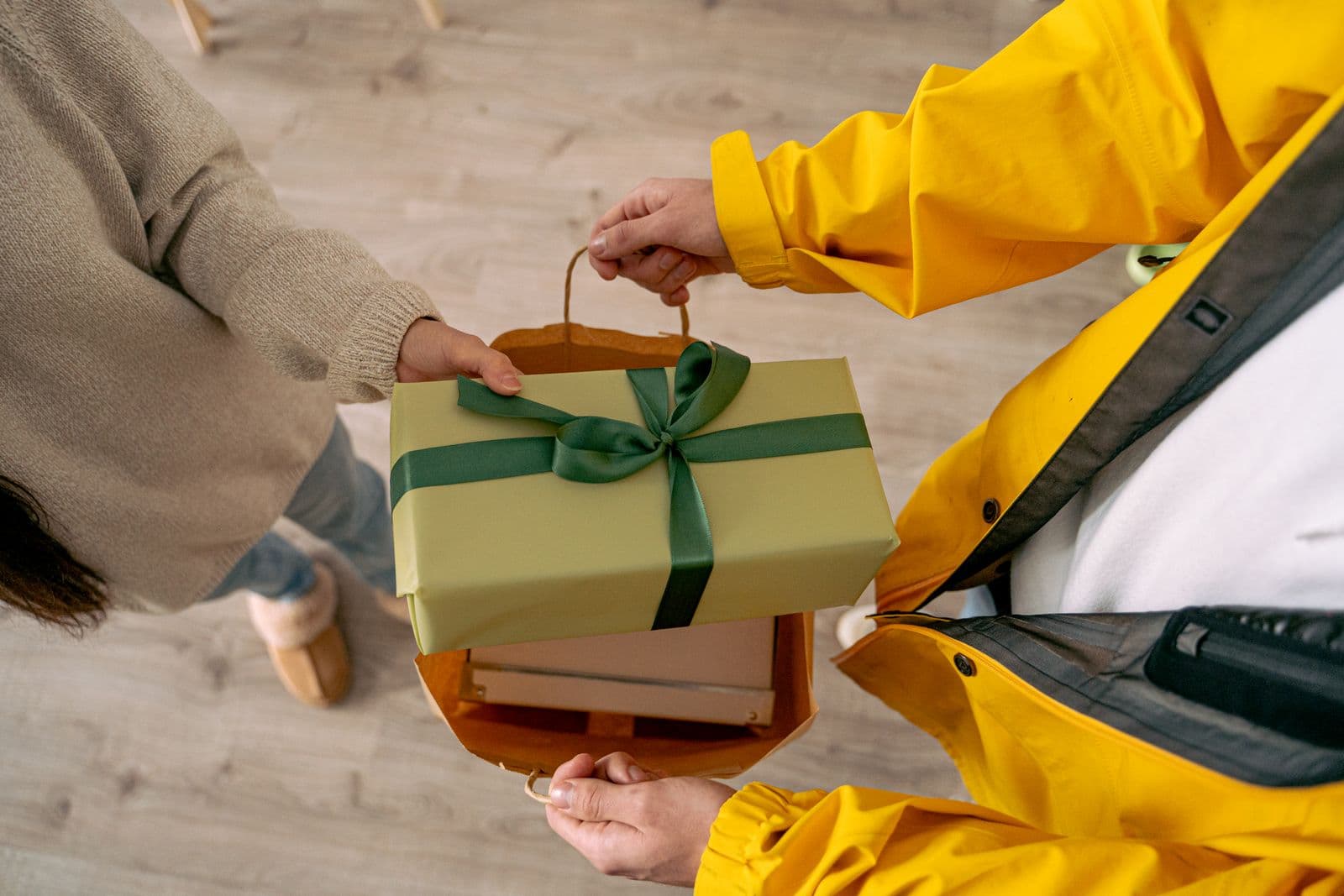 Een bezorger overhandigt aan de voordeur een netjes ingepakt cadeau in een papieren tas aan een blij verraste ontvanger