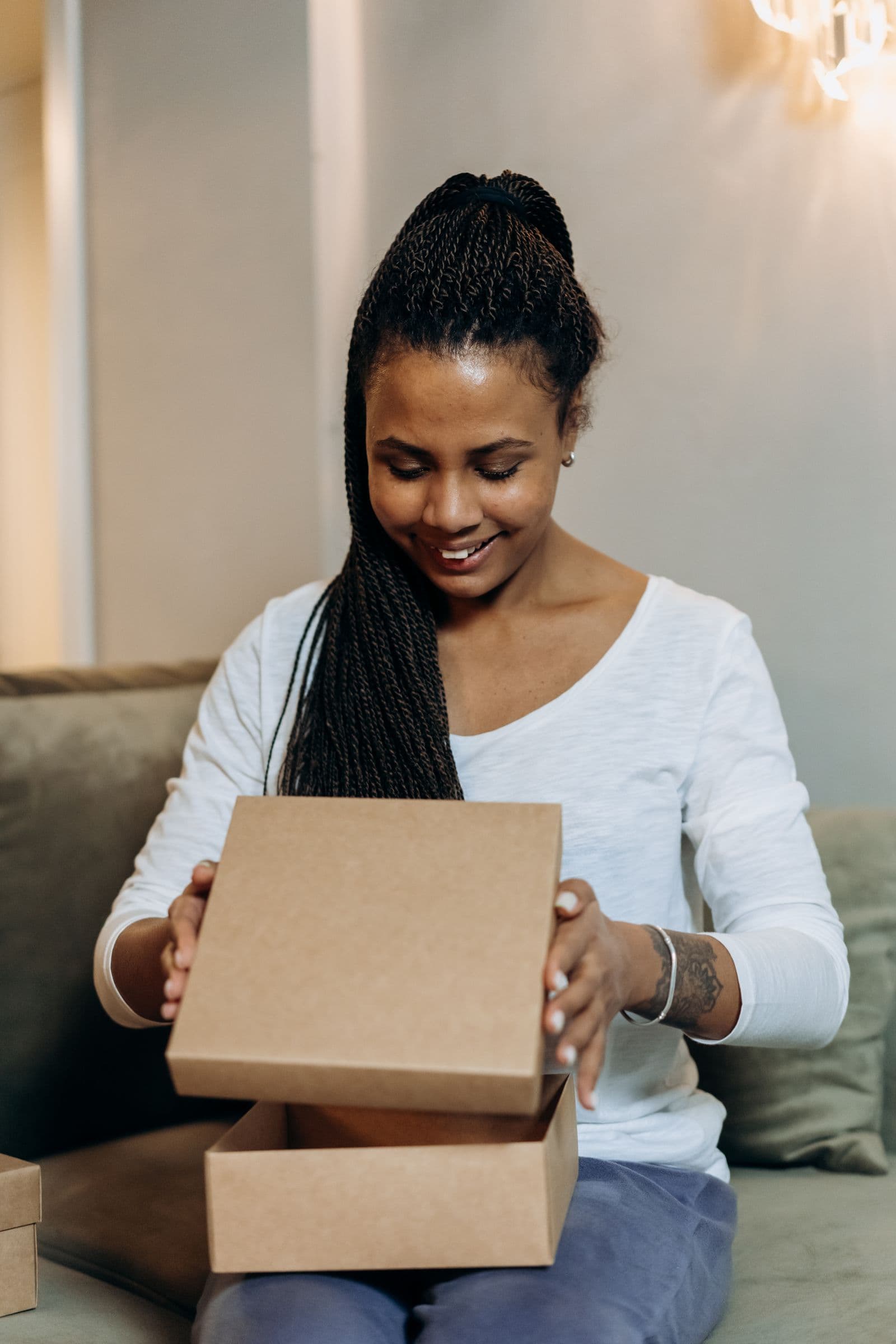 Een blij verraste vrouw pakt in haar woonkamer een onverwacht bezorgd cadeaupakketje uit met een grote glimlach
