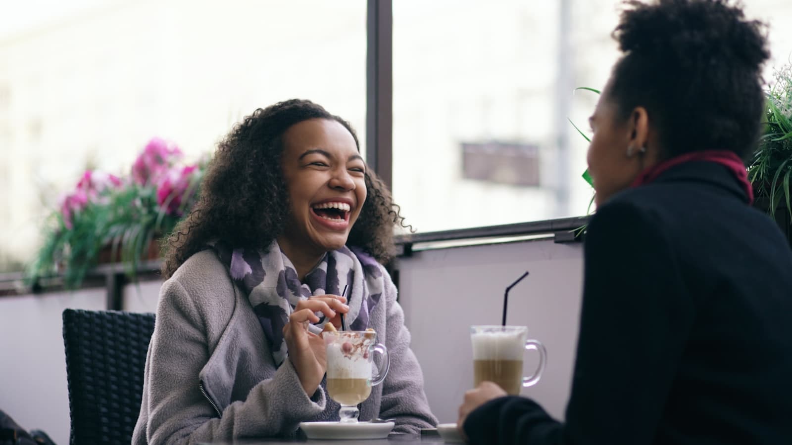 Twee vriendinnen lachen samen aan een cafétafel met een warme koffie, een beeld bij een cadeau voor je beste vriendin