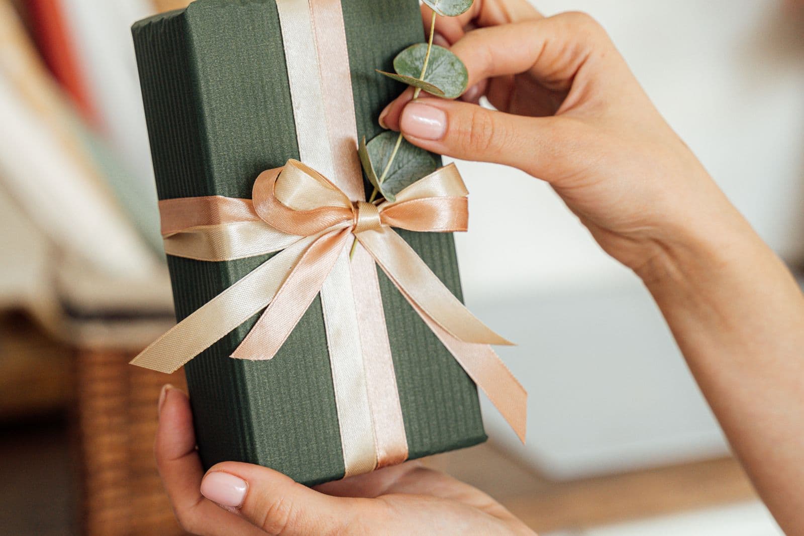 Twee handen houden een zorgvuldig ingepakt cadeau met lint vast, een beeld bij een verrassing voor een vrijgezellenfeest