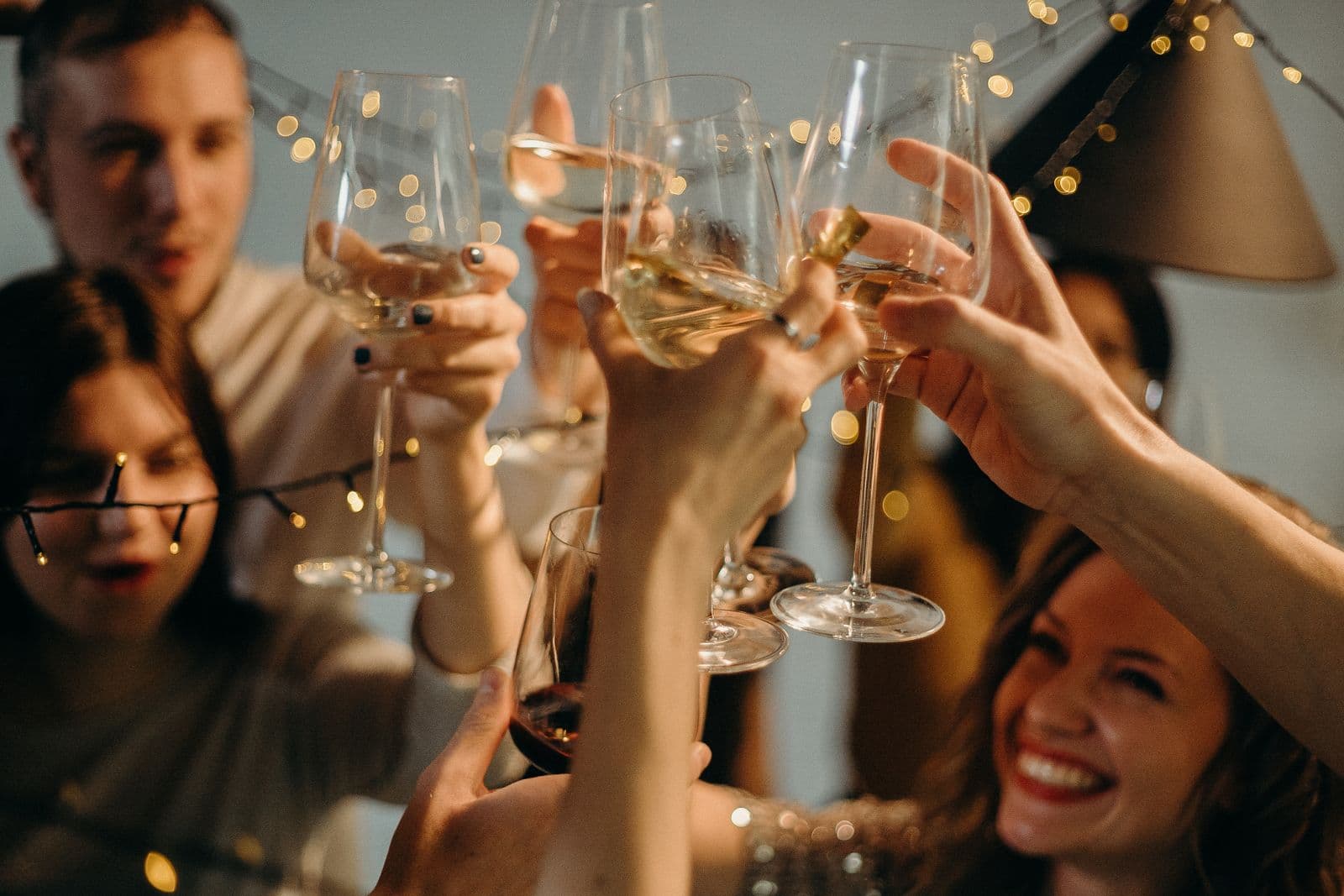 Een groep vrienden proost lachend met glazen onder lichtjes tijdens een feestelijke avond, een beeld bij een vrijgezellenfeest