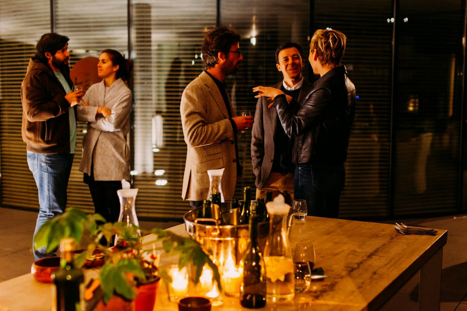 Collega’s staan ontspannen samen te praten met een glas in de hand tijdens een borrel op kantoor in de avond, een warm beeld bij de vrijdagmiddagborrel