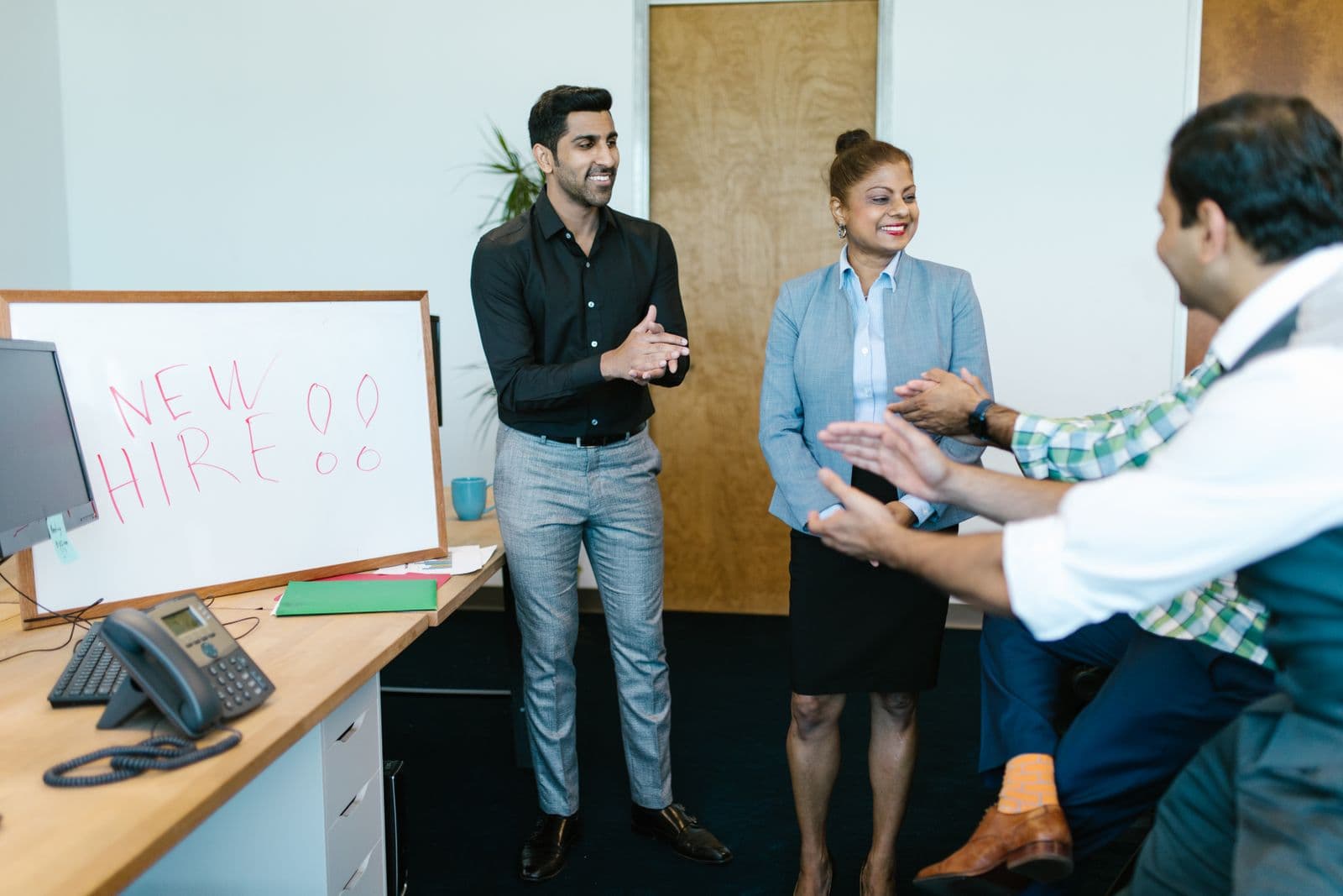 Collega's applaudisseren en verwelkomen een nieuwe medewerker bij een whiteboard met de tekst new hire op kantoor, een warm beeld bij het welkom heten van een nieuwe collega